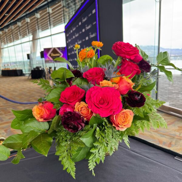 Jewel-toned live flower arrangement with vibrant roses, ranunculus, and greenery for a corporate event reception.