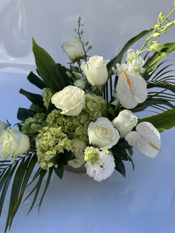 Tropical white floral arrangement with roses, hydrangea, orchids, anthurium, and palm leaves in a modern design.