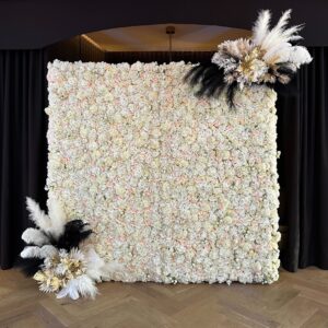 White faux floral wall with soft flowers and dramatic black, white, and gold feather arrangements.