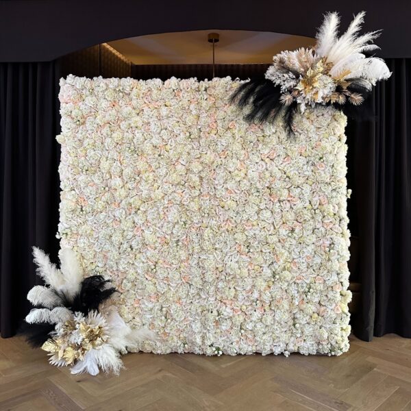 White faux floral wall with soft flowers and dramatic black, white, and gold feather arrangements.