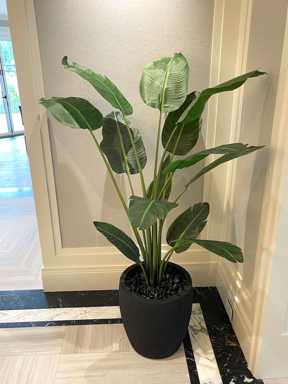Artificial travelers palm tree in a black decorative pot in a residential hallway