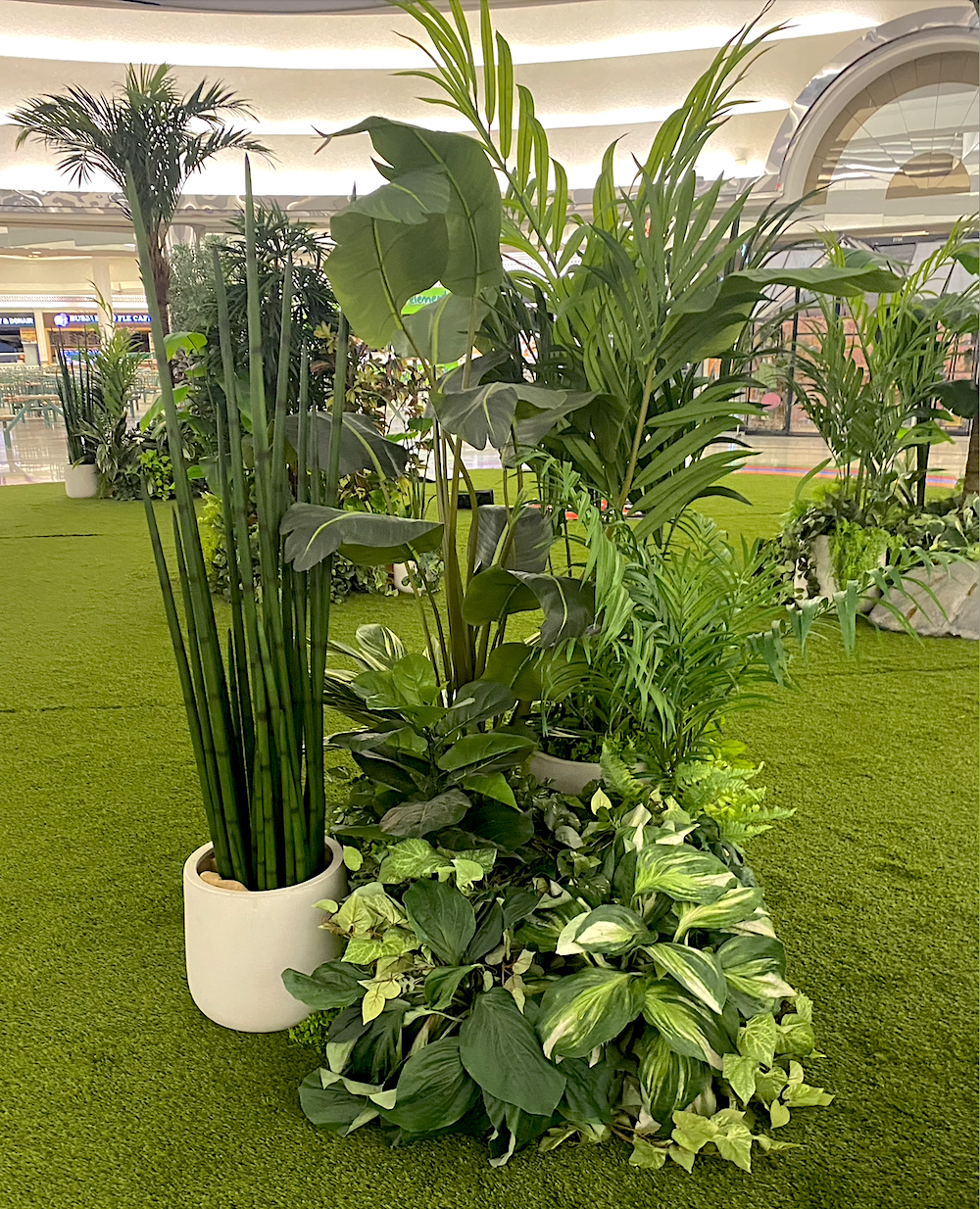 Artificial tropical plants displayed on green artificial turf in the middle of a mall.