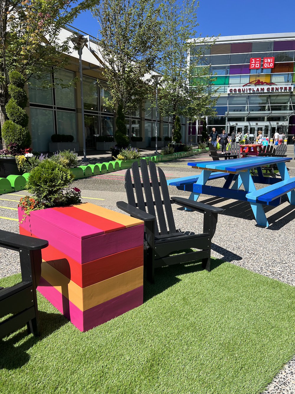 Wooden patio cubes and picnic tables painted in rainbow colours to create fun and festive seating areas at the outdoor plaza at Coquitlam Centre.