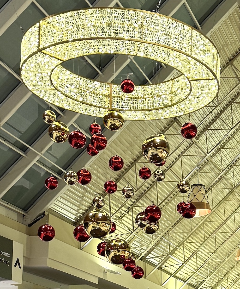 Greenscape Design's festive holiday decor at Coquitlam Centre features an overhead ornament chandelier adorned with hanging red and gold baubles.