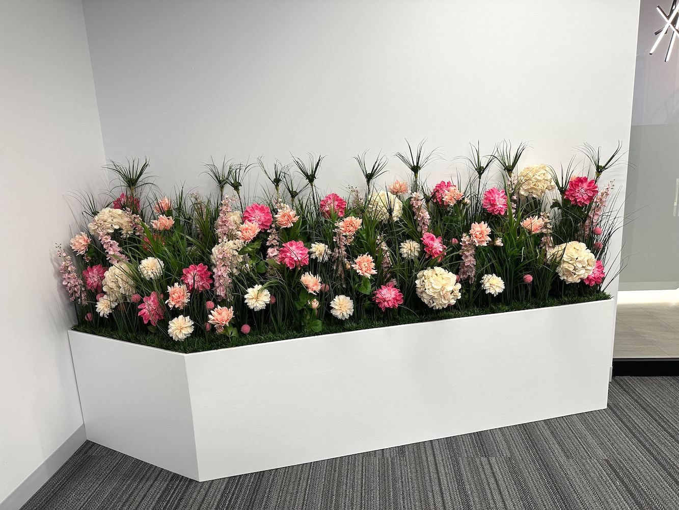 Custom artificial floral planter by Greenscape Design at Lux Skin Lab in Vancouver, featuring pink, white, and cream florals and greenery in a white planter against a white wall.