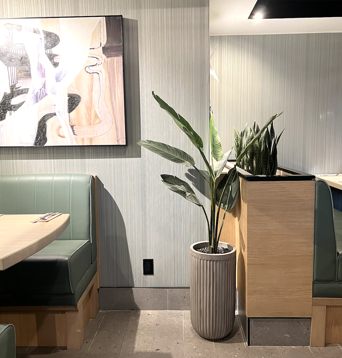 Modern artificial traveler palm in planter next to banquette seating at a restaurant in Vancouver.