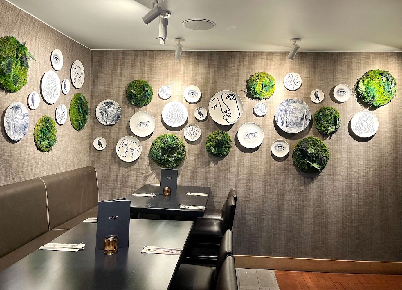 Custom moss wall art circle frames interspersed between decorative ceramic plates on a restaurant wall.