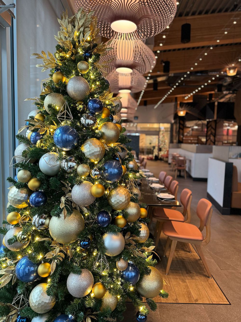 Blue and Gold Christmas tree by a restaurant entrance. Elegant and timeless restaurant Christmas decor by Greenscape Design in Vancouver.