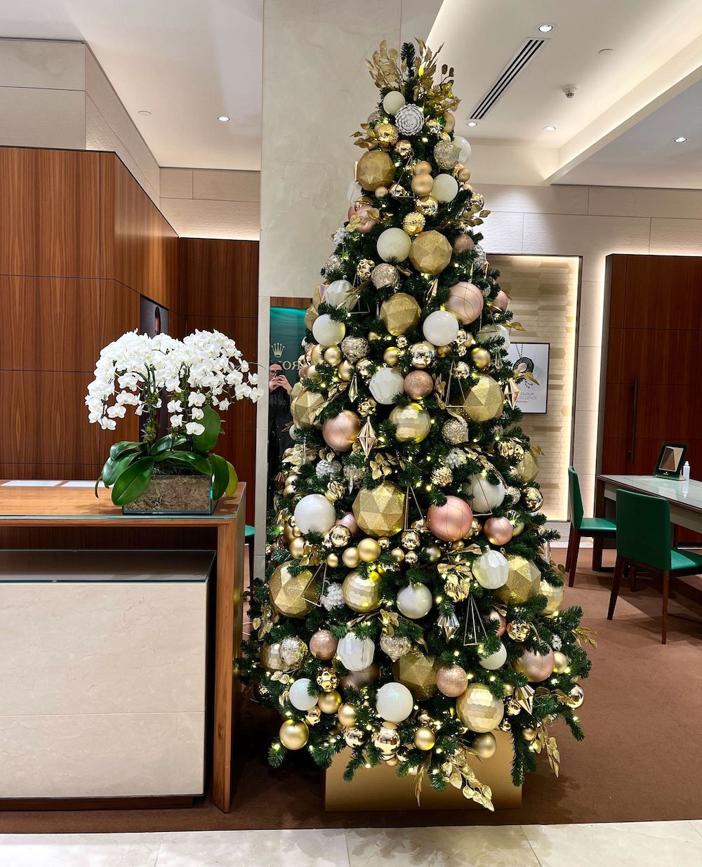 9' tall christmas tree decorated in a rose gold, gold, and white decor theme in a commercial space next to a desk.