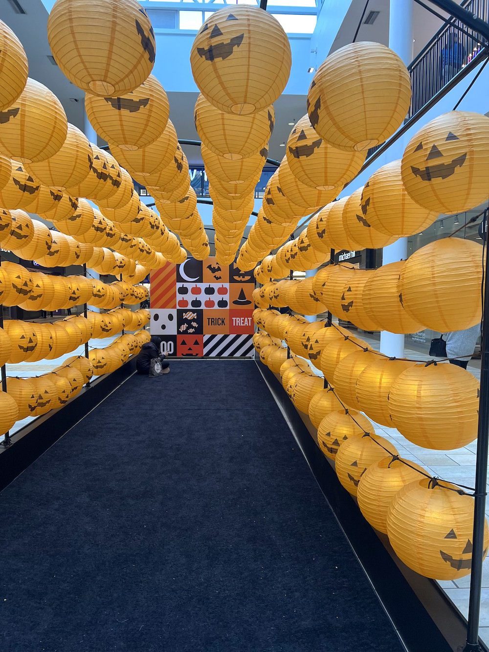 Hundreds of orange pumpkin lanterns creating an interactive Halloween tunnel display at The City of Lougheed by Greenscape Design.