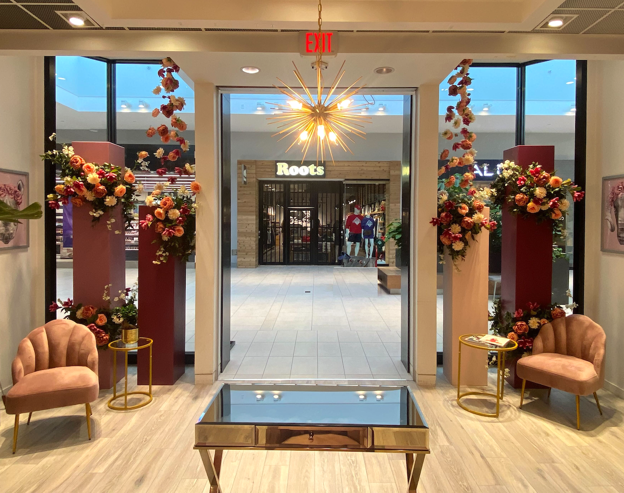 Colourful custom designed florals adorn deep pink and burgundy pillars with a floral chandelier at Willowbrook Mall storefront window for a photo op.