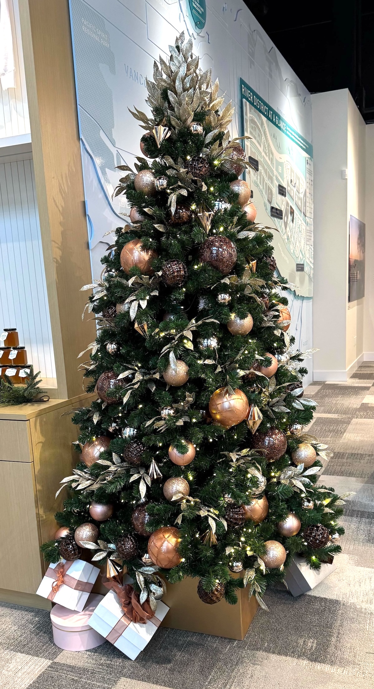 Artificial Christmas tree decorated with copper, bronze, and gold ornaments, featuring a shimmering topper and wrapped gift boxes at the base.