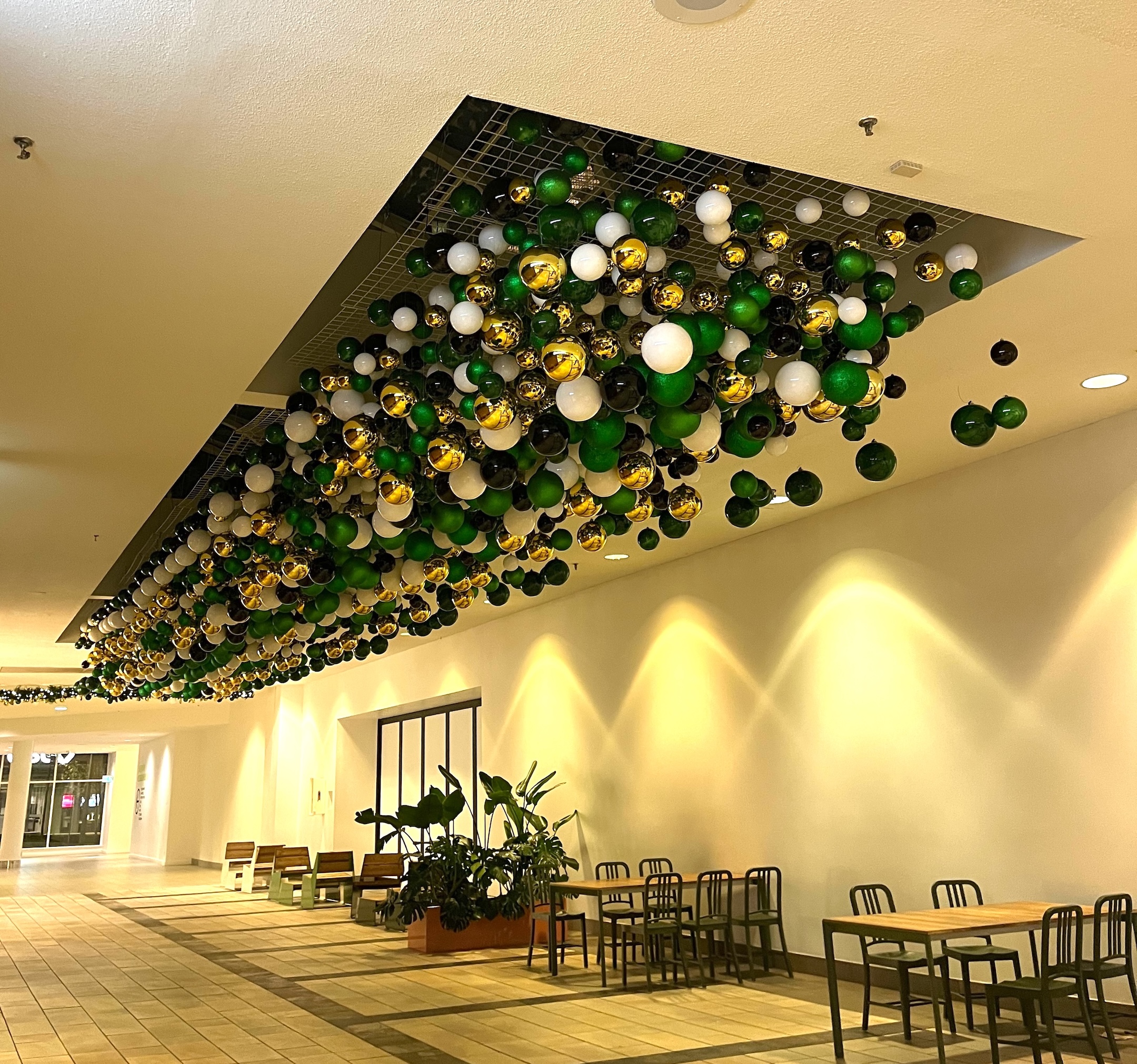 Suspended ceiling décor featuring green, gold, black, and white baubles in a dynamic arrangement, creating a festive atmosphere in Lougheed Mall.
