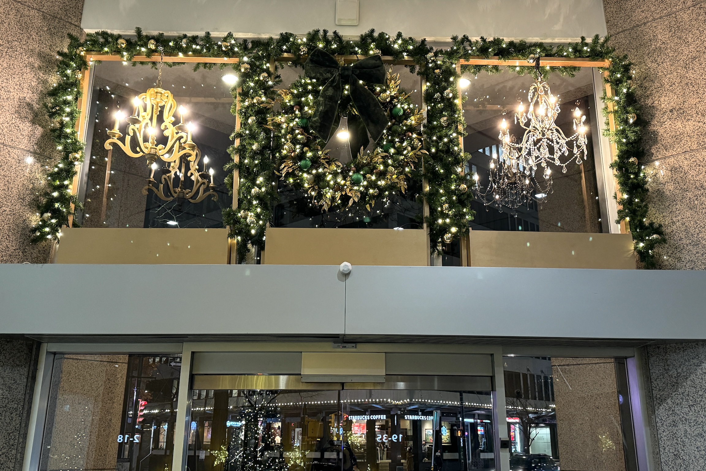 Festive window display with illuminated green and gold wreath, lush garlands, and elegant chandeliers, creating a captivating holiday scene at Park Place.