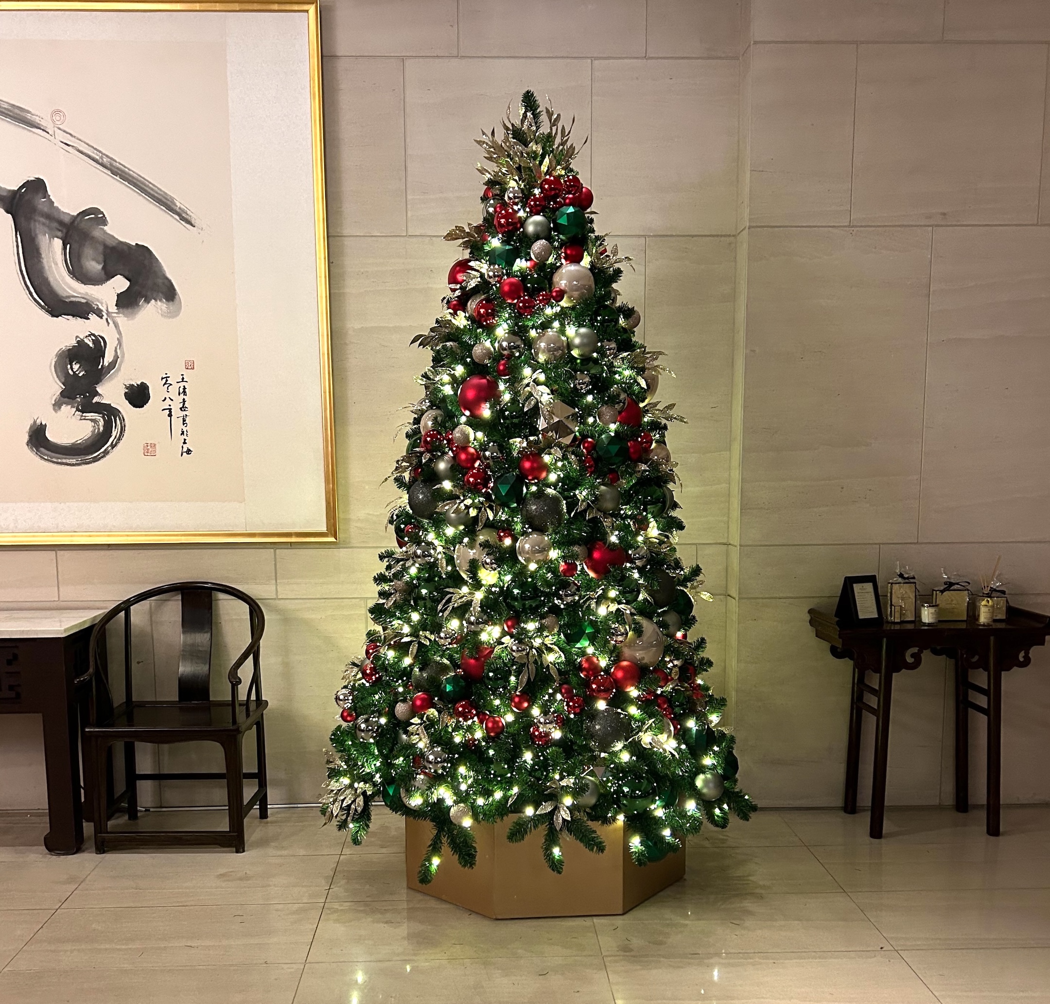 Elegant Christmas tree decorated with red, green, and oat ornaments, warm white lights, and a golden base, displayed in the Shangri-La Vancouver Lobby.