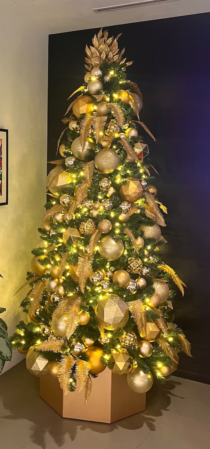 Stunning Christmas tree adorned with monochromatic gold ornaments, geometric designs, and warm lights, set in an office lobby interior.