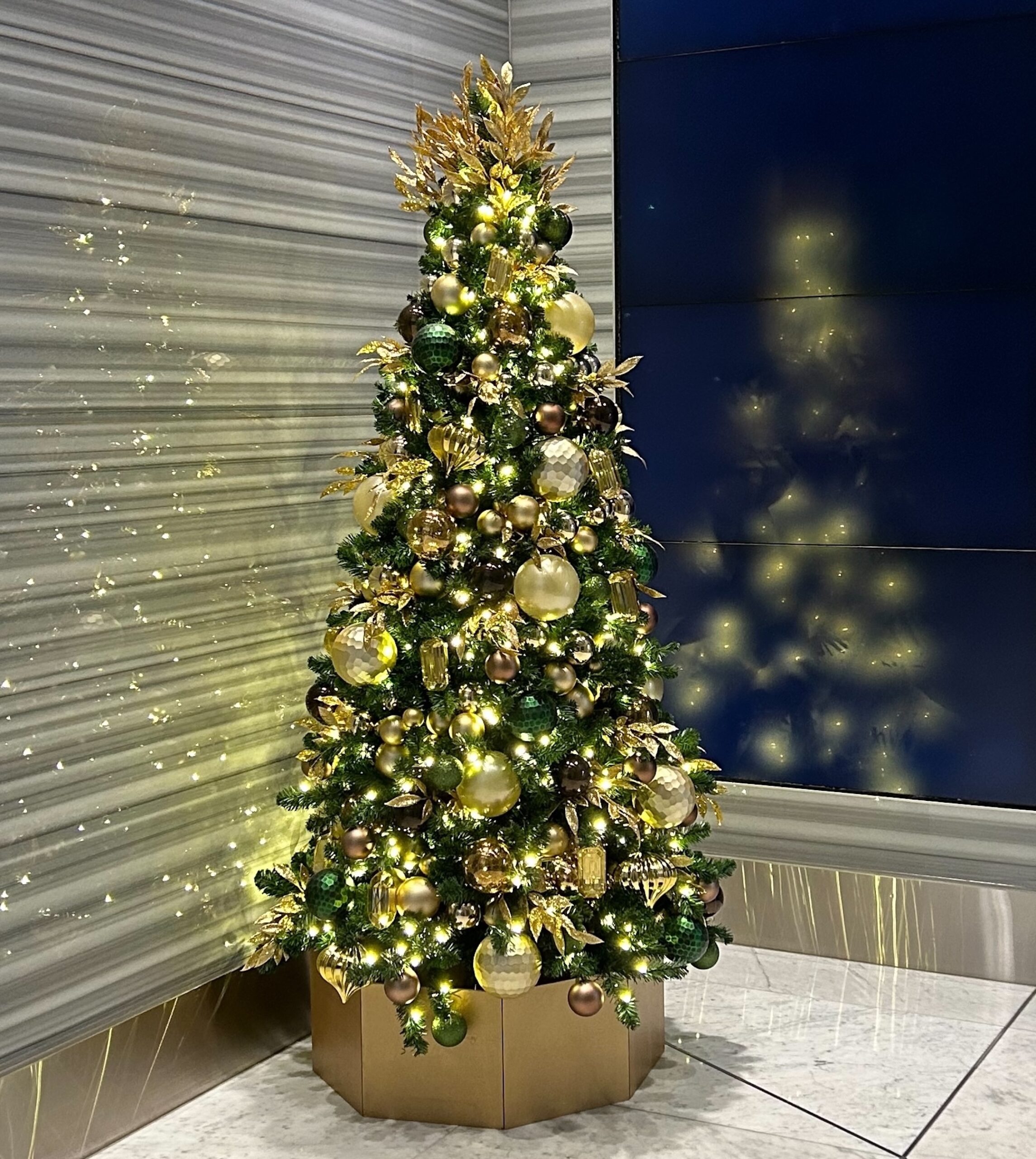 Artificial Christmas tree adorned with gold, bronze, and green ornaments, complemented by warm lighting and elegant detailing, displayed in Vancouver office lobby.