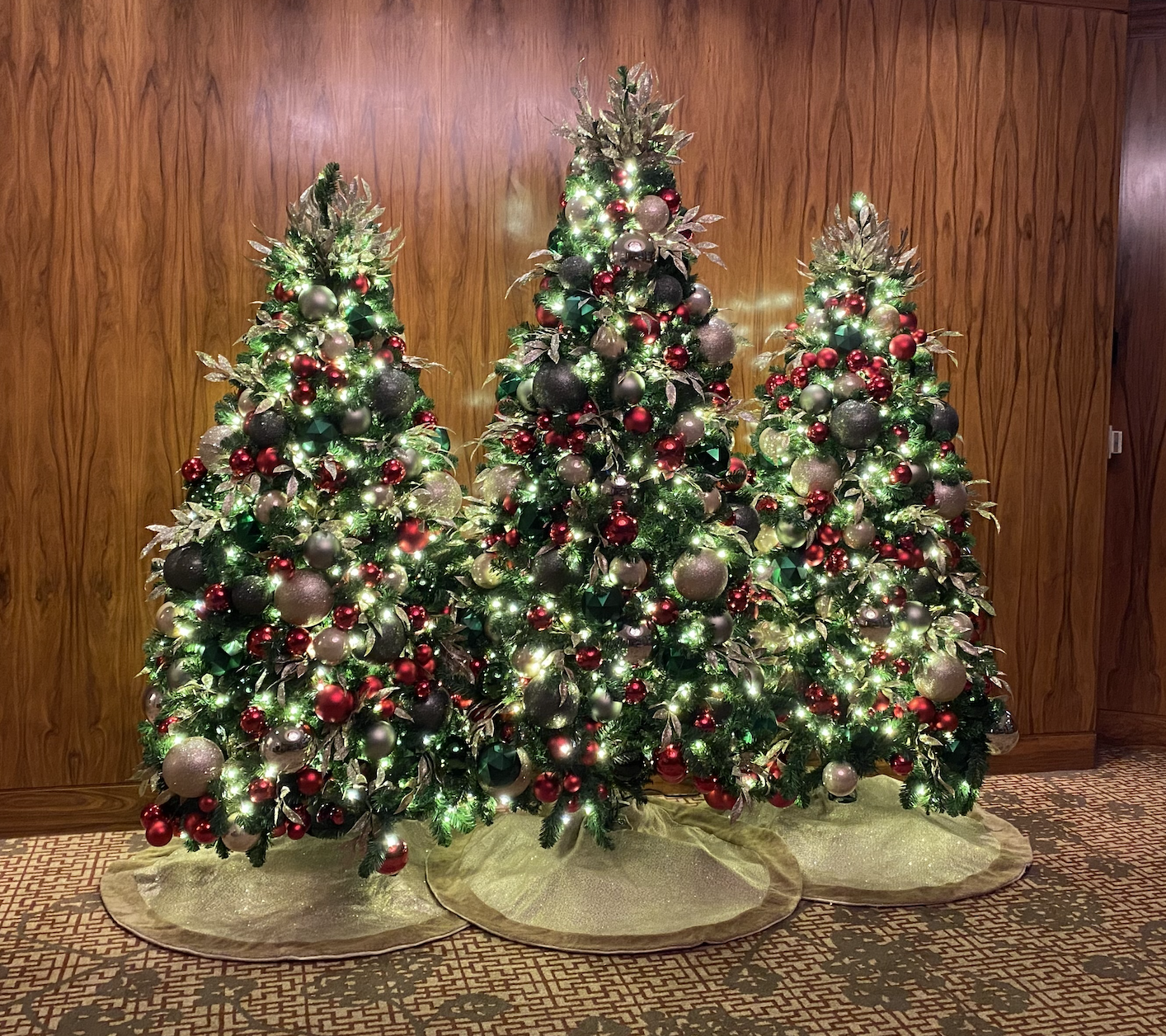 Set of three Christmas trees decorated with red, green, and oat ornaments, illuminated with warm white lights, displayed at the Shangri-La Hotel Vancouver.