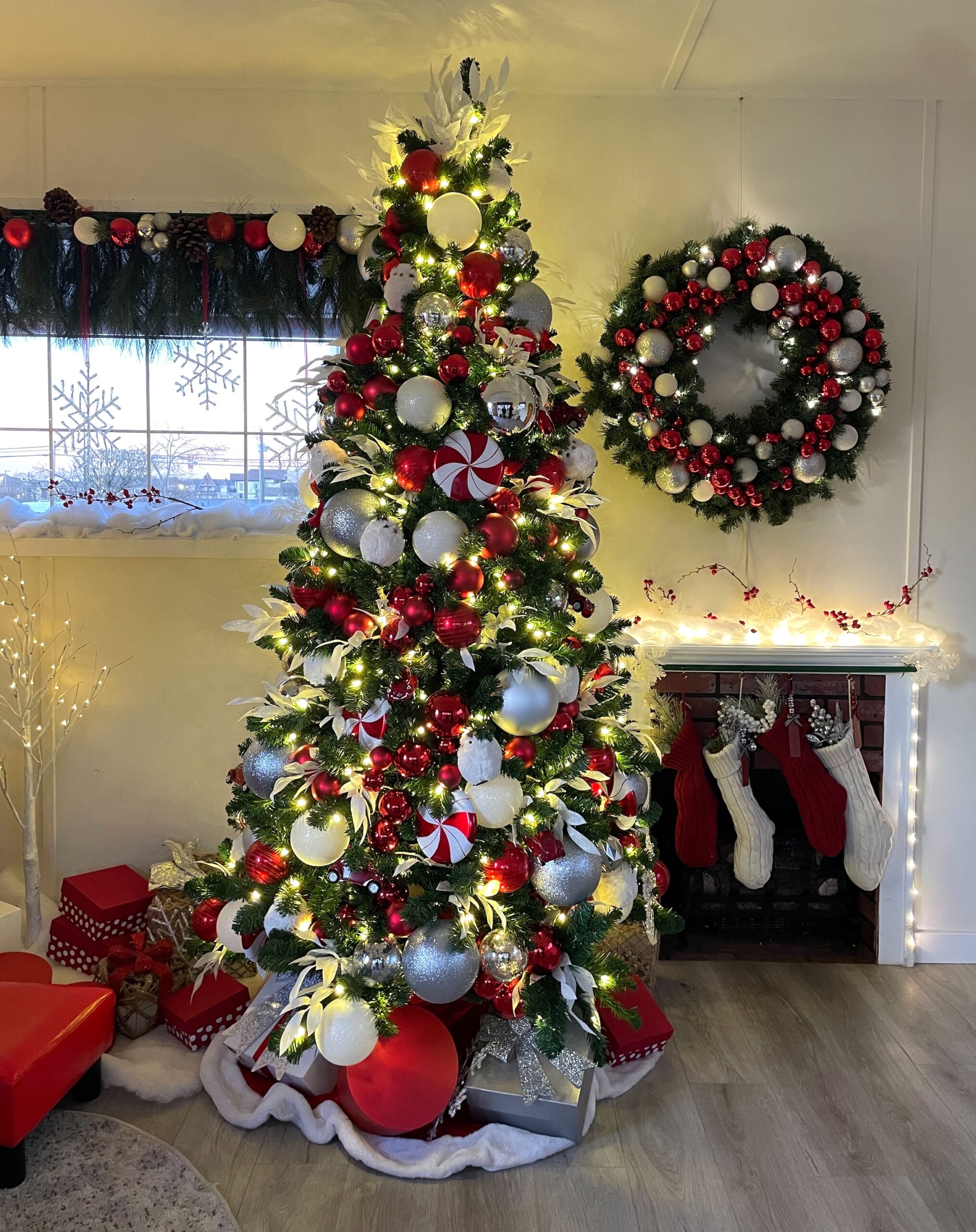 Christmas tree decorated in red, white, and silver ornaments with candy cane accents, accompanied by a matching wreath and fireplace setup for a Santa photo op.