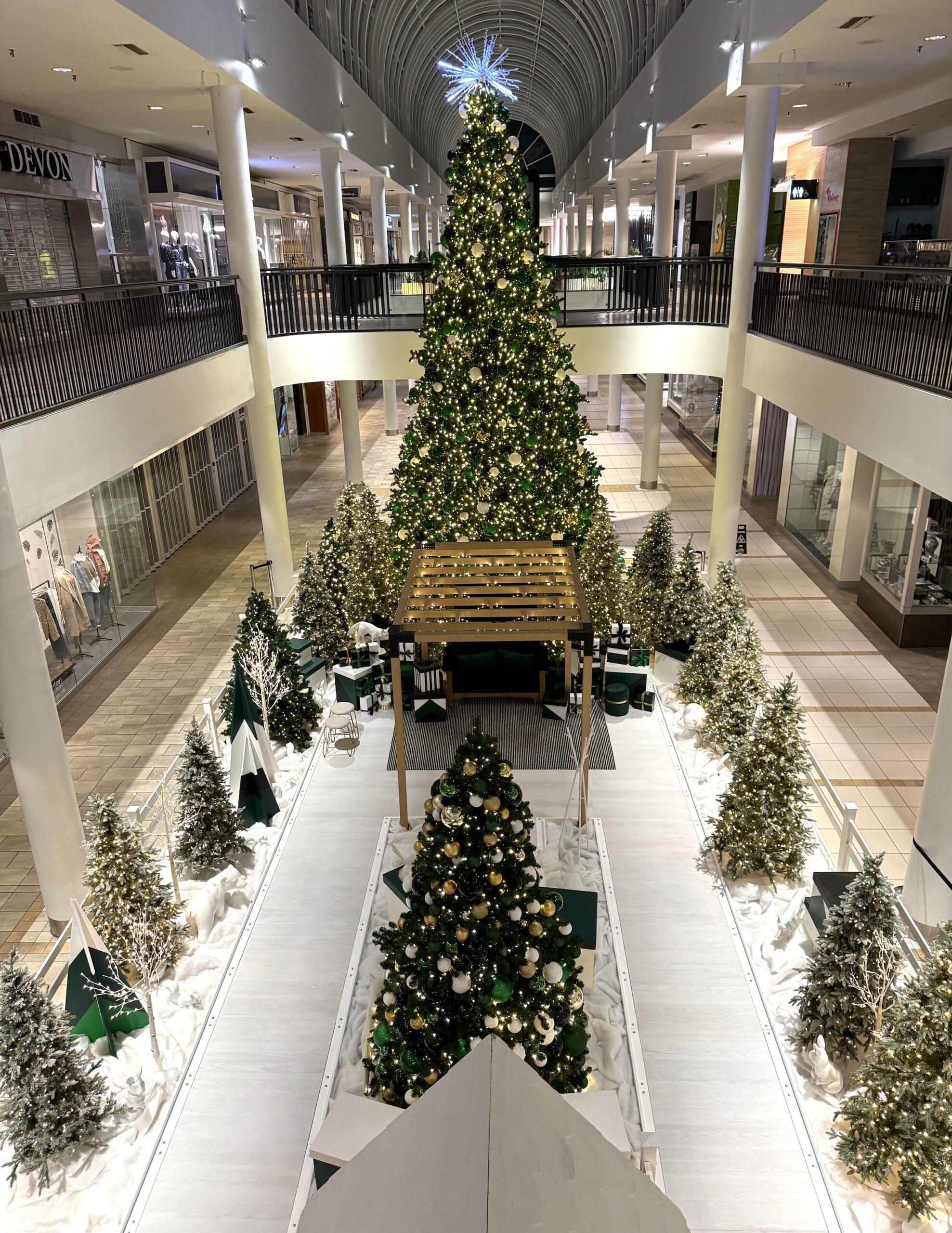 Large-scale Santa set with a majestic Christmas tree centerpiece, surrounded by smaller decorated trees, illuminated displays, and a festive seating area in Lougheed shopping mall.