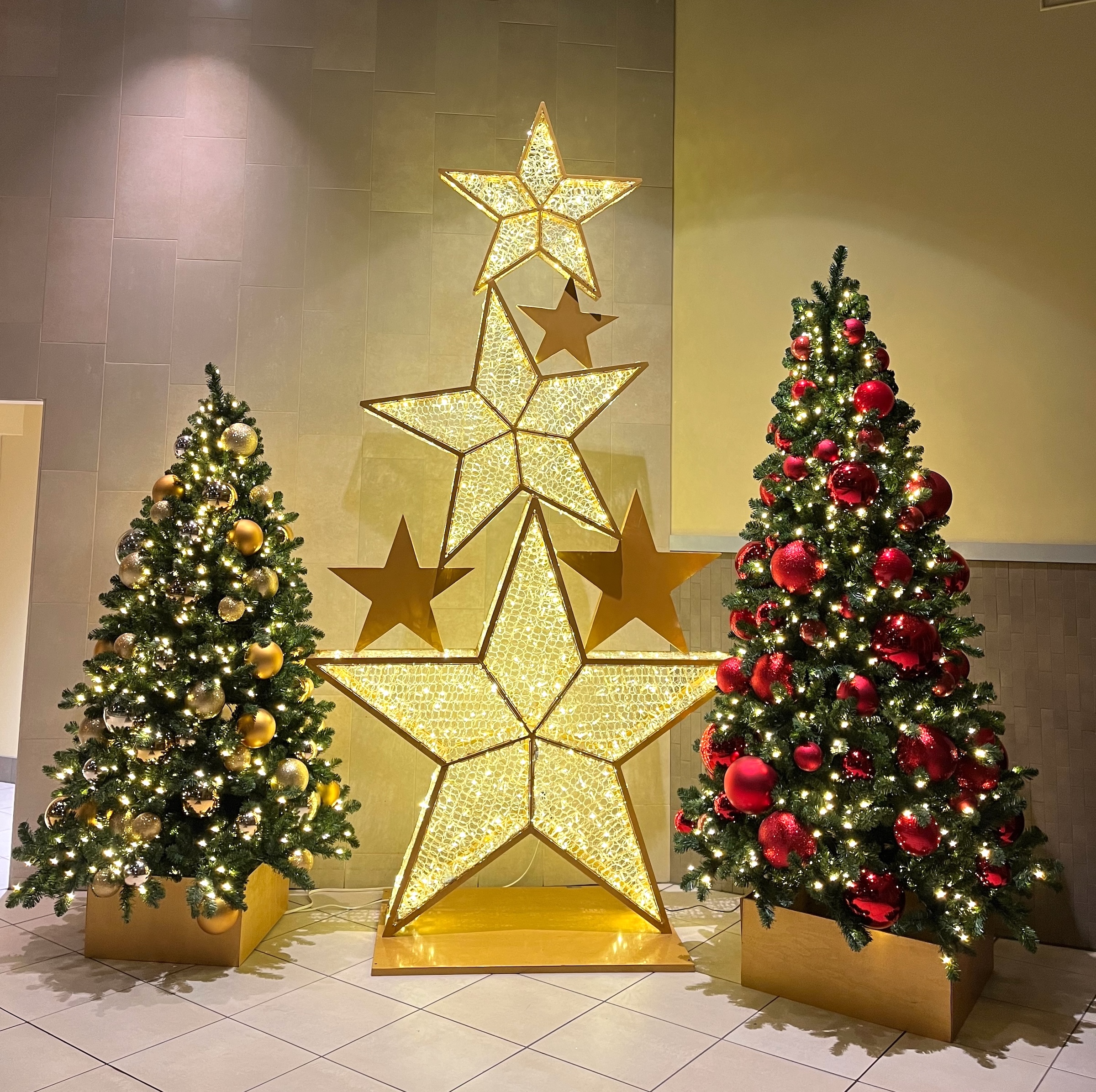Christmas display with gold and red decorated trees, accompanied by illuminated star sculptures, found in Coquitlam Centre entrance lobby.