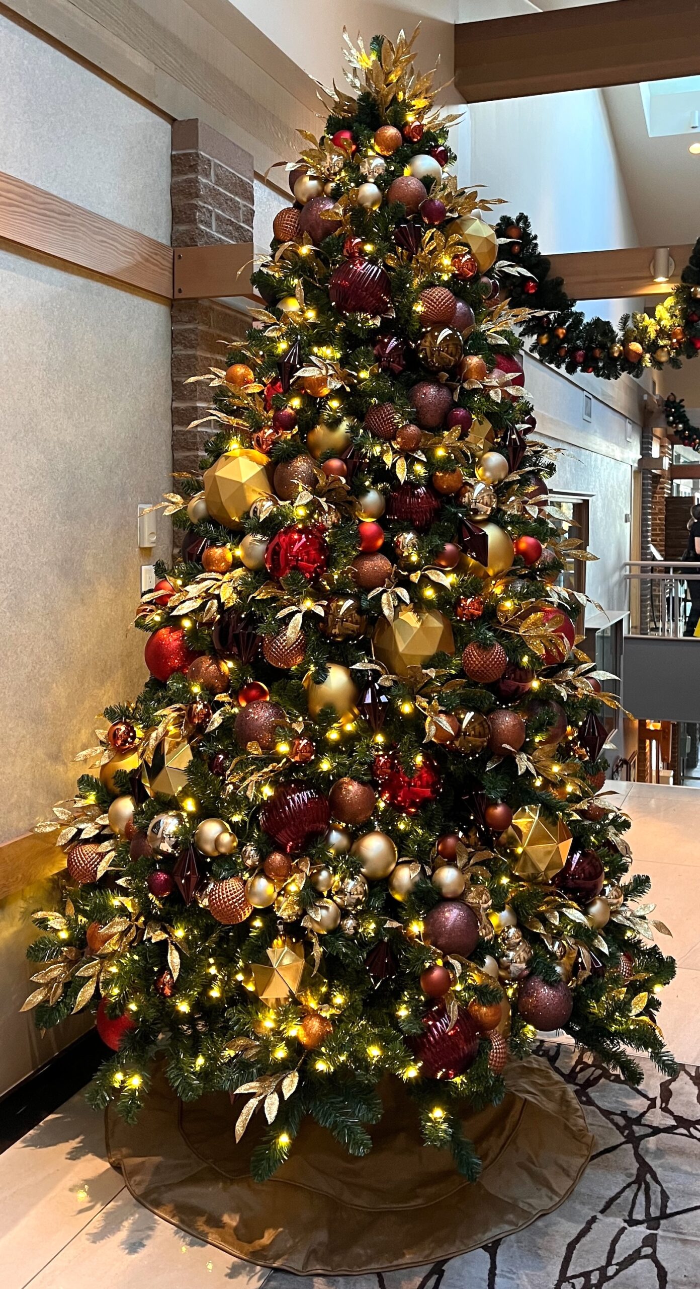 Classic Christmas tree adorned with red, gold, and bronze ornaments, warm lights, and lush greenery, displayed in a festive golf course resort lobby.