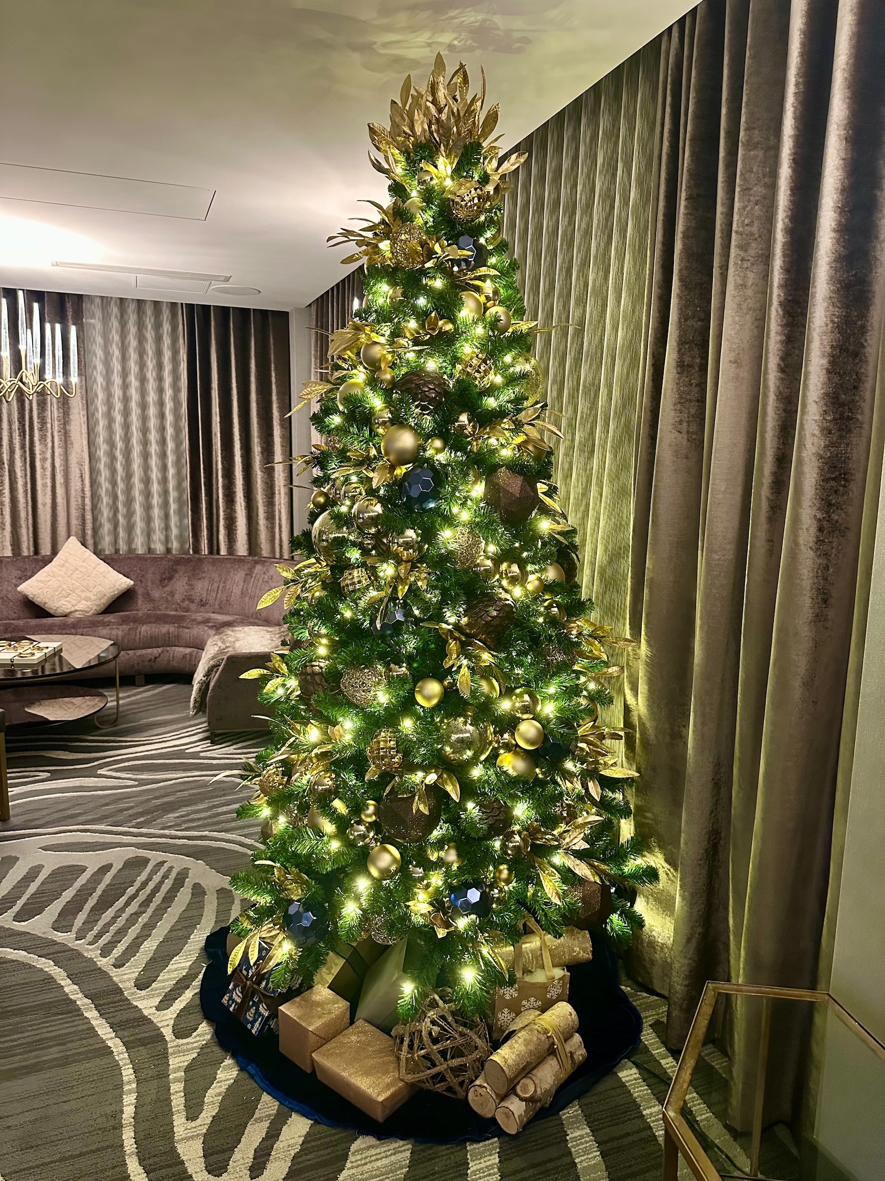 West Coast-inspired Christmas tree with gold ornaments, pinecones, natural elements, and warm lighting, set in a luxurious hotel lounge.