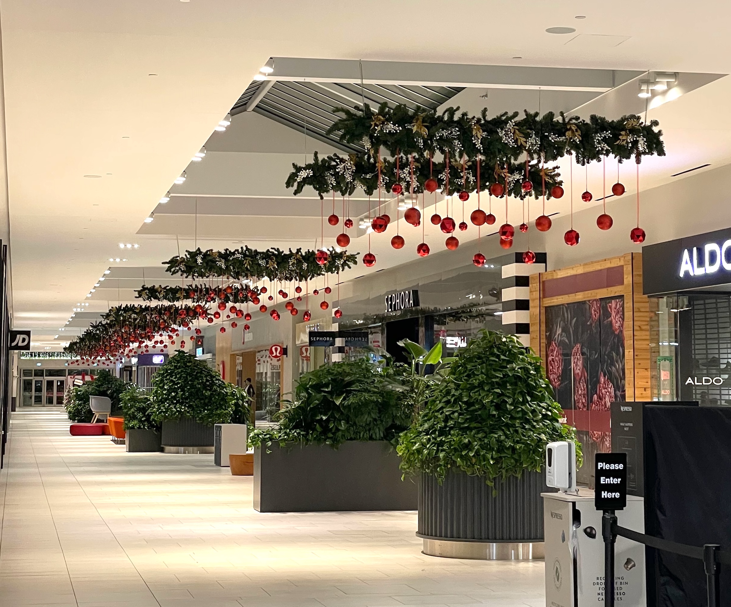 Overhead Christmas garlands with hanging red ornaments at Willowbrook Mall in Surrey, BC, designed by Greenscape Design.