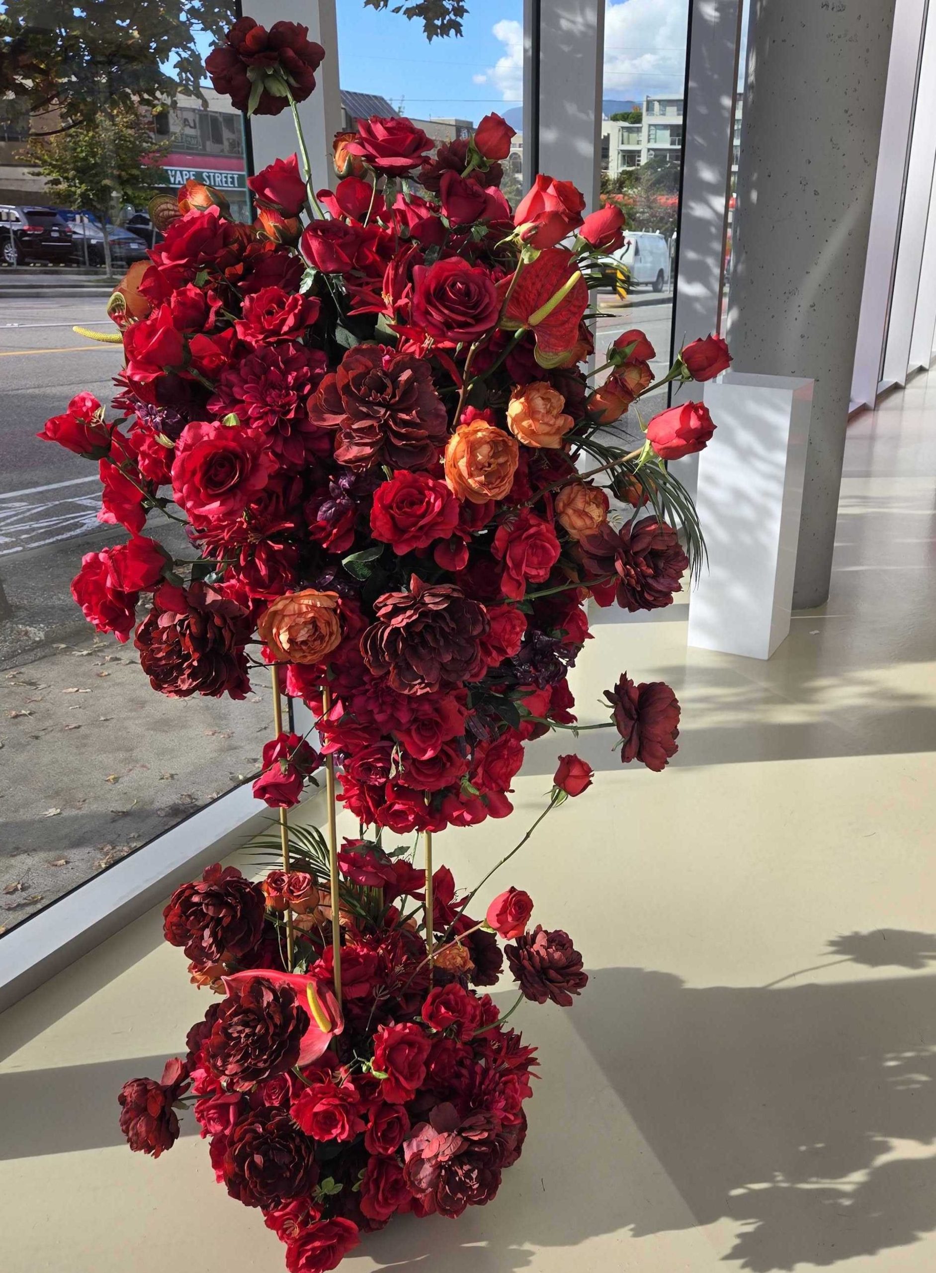 Striking artificial red floral arrangement featuring roses and peonies in deep crimson and burnt orange hues, designed for event rentals.