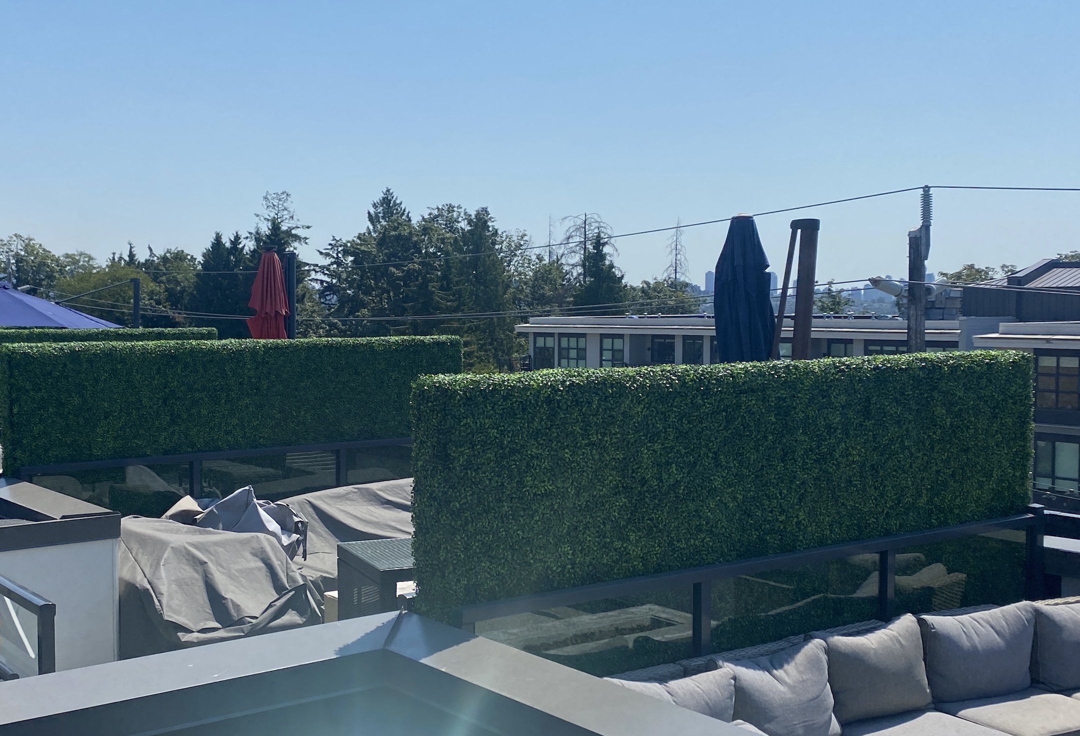 Fake boxwood hedge privacy walls installed on a modern condo rooftop, providing green screening with a cityscape view.