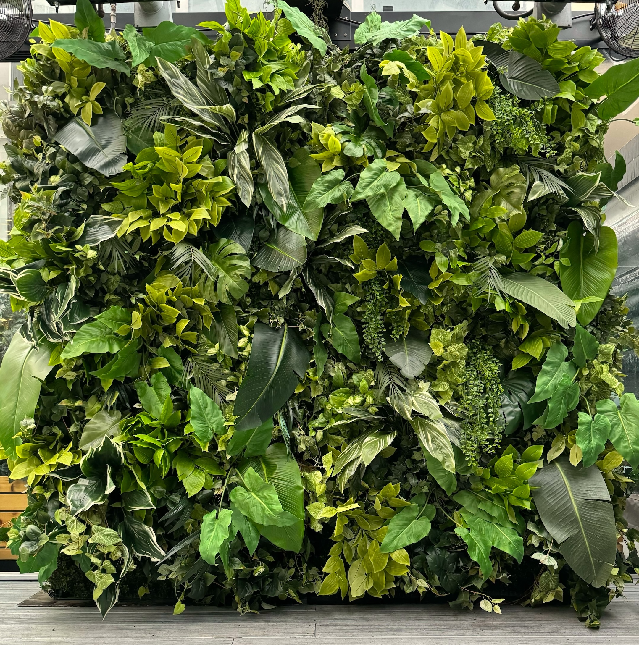 Lush artificial green wall featuring a mix of tropical and variegated foliage, creating a vibrant and textured event backdrop.