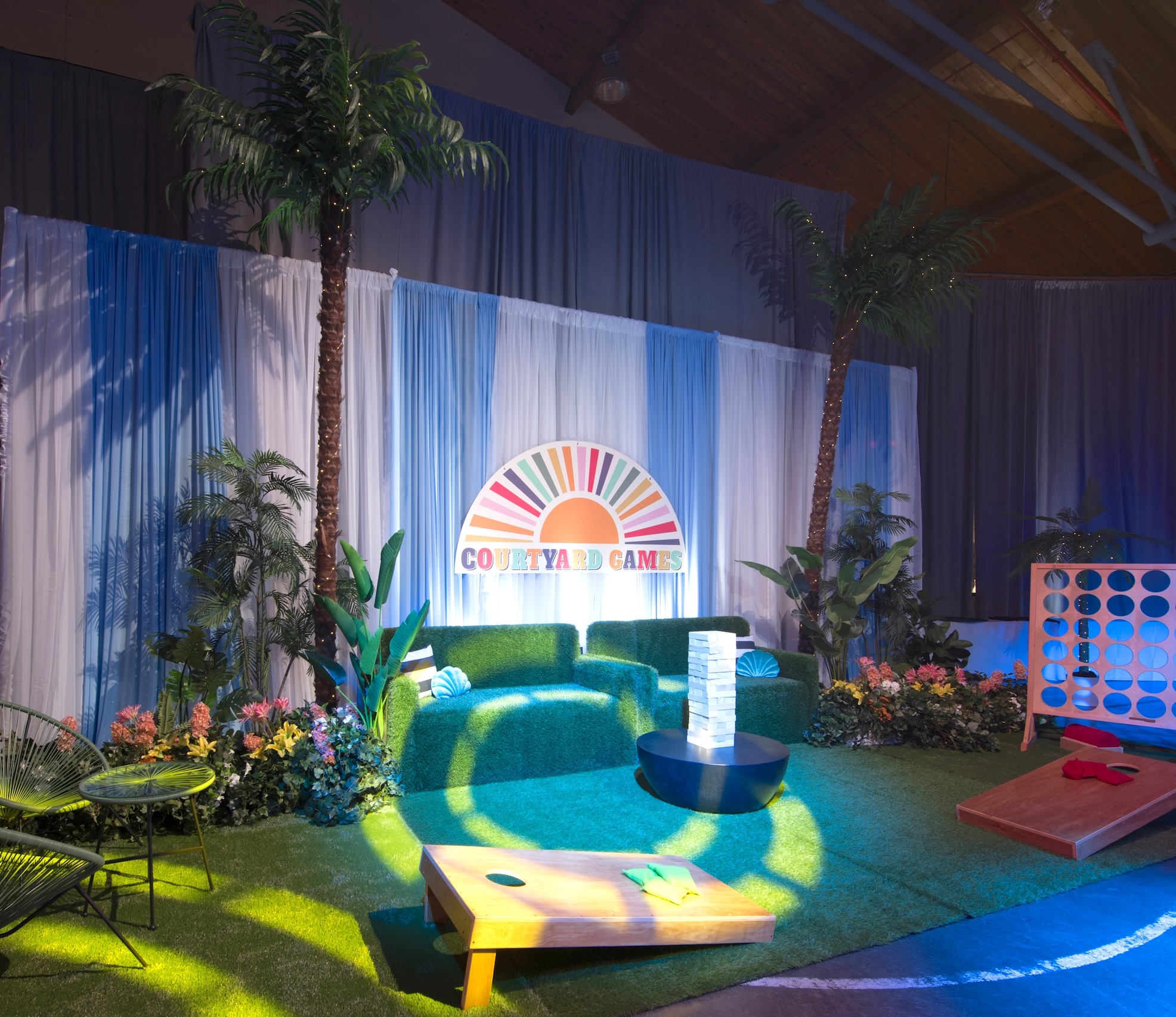 A vibrant event setup featuring artificial palm trees, lush greenery, and interactive courtyard games.