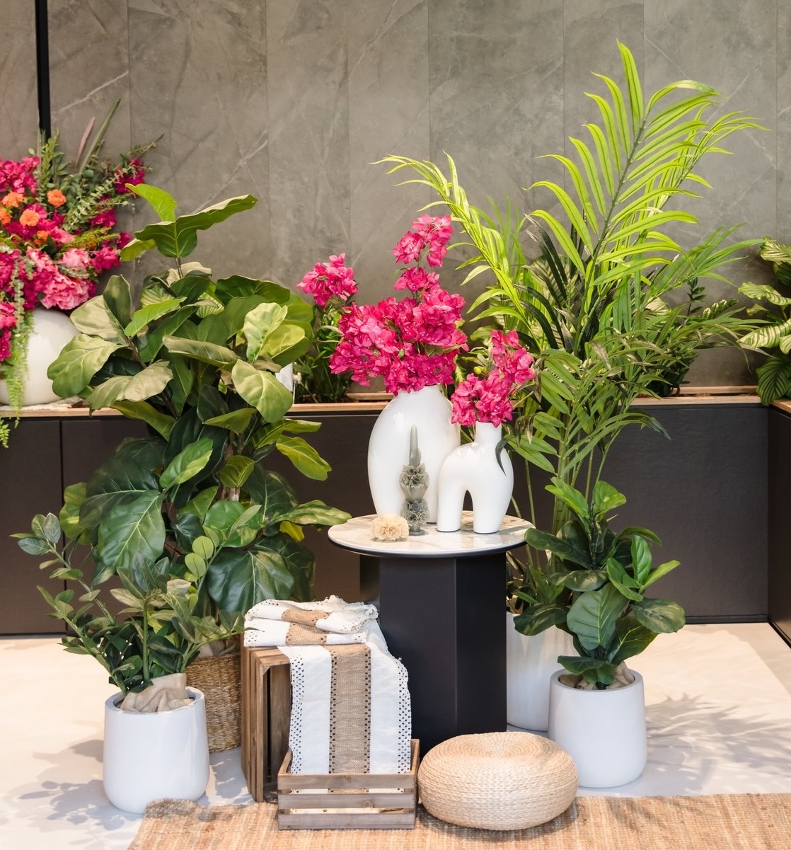 A stylish corporate event display featuring artificial plants, vibrant pink flowers, and modern décor elements.