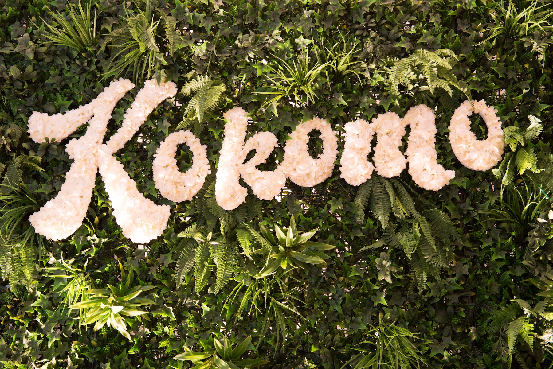 A lush tropical green wall with custom floral lettering spelling "Kokomo," creating a vibrant event backdrop.