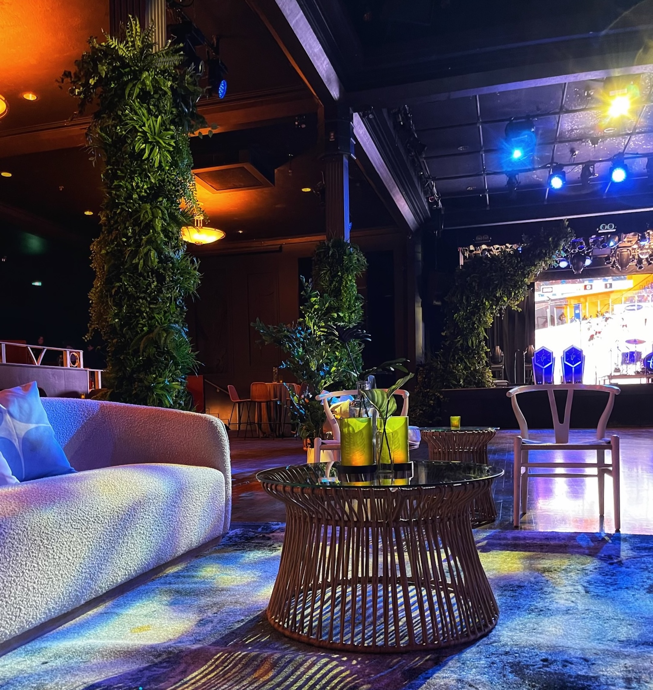 A stylish corporate event setup at Commodore Ballroom featuring lush greenery, modern lounge seating, and a stage backdrop.