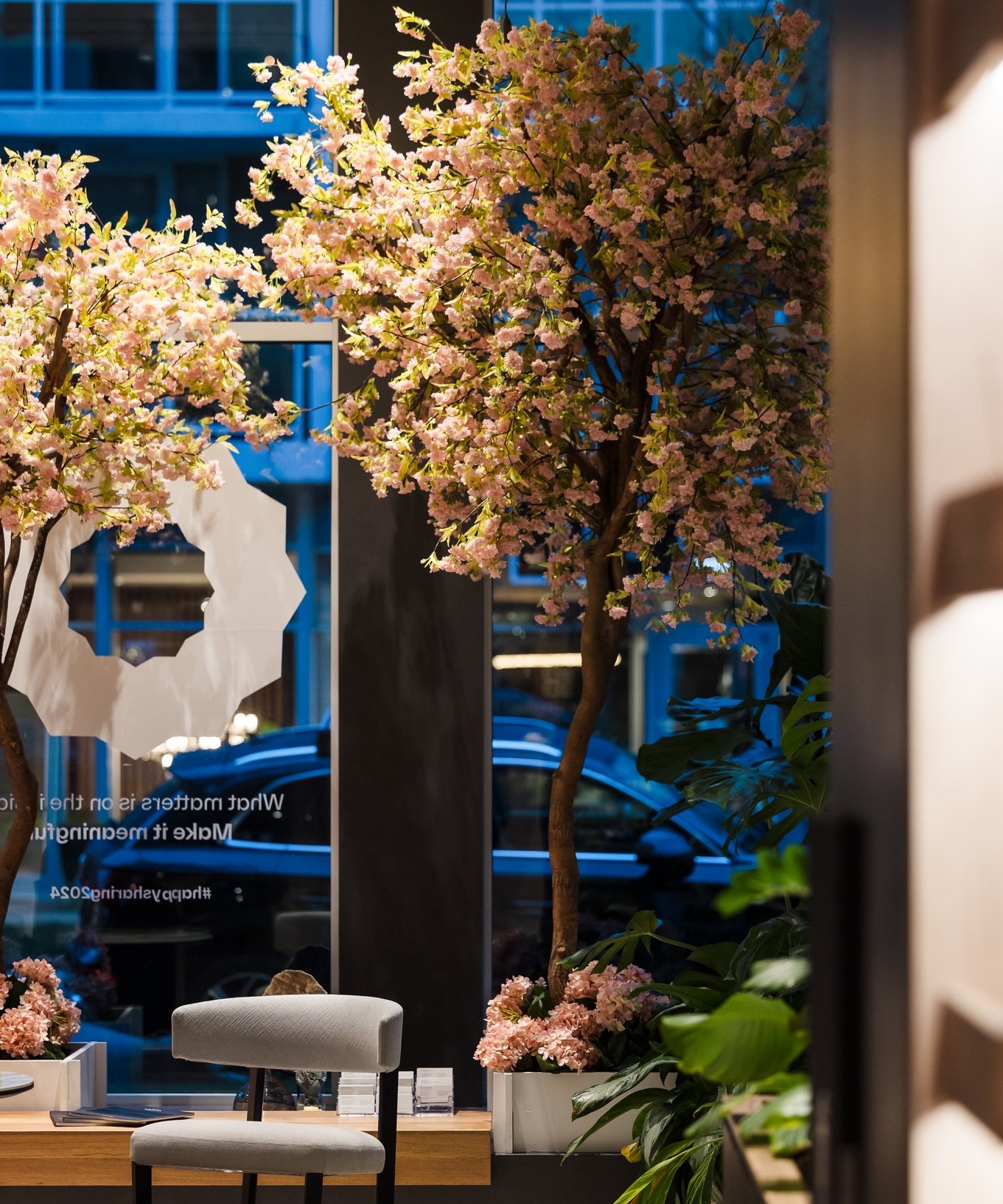 A modern corporate event space featuring artificial cherry blossom trees and lush greenery, creating a sophisticated ambiance with spring themed event décor