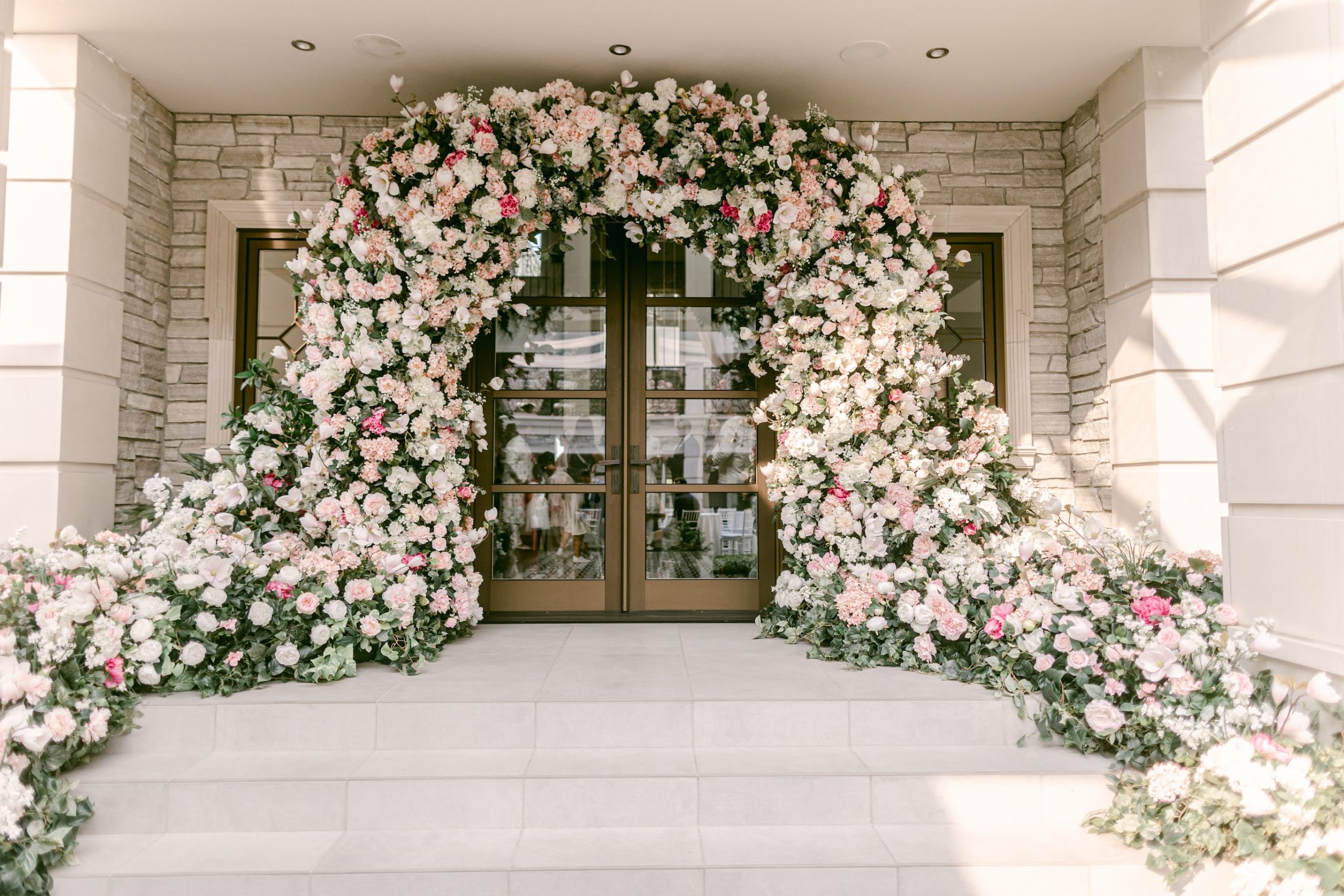 A grand floral arch in soft pink and white blooms, cascading elegantly over a doorway, creating a breathtaking entrance for a luxury wedding.