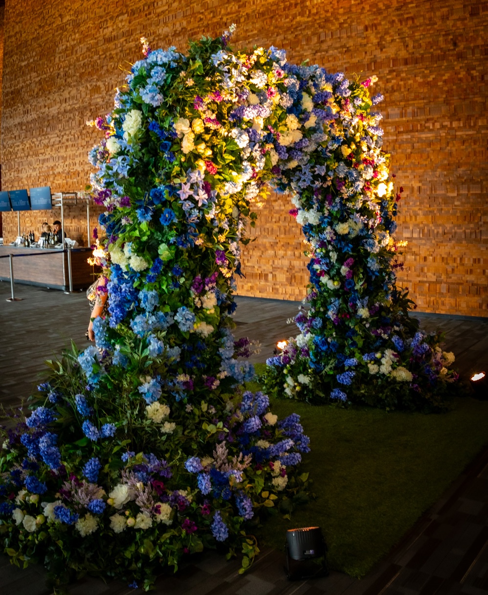 A grand artificial floral entrance arch adorned with lush blooms, creating an elegant statement for a corporate event.