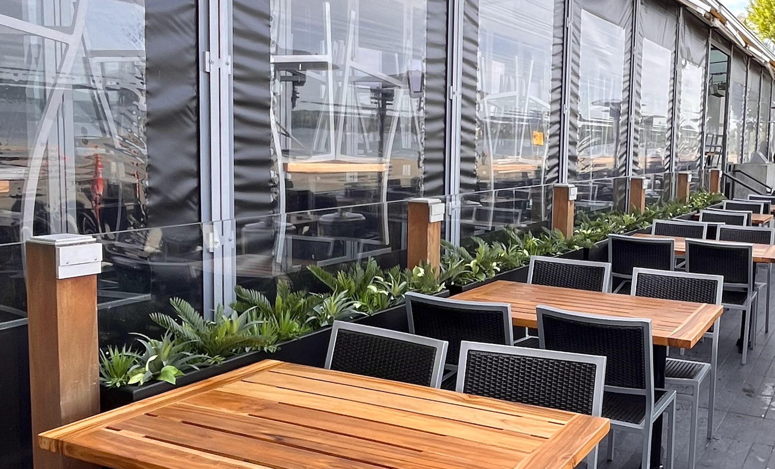 Restaurant patio lined with sleek black planters filled with lush faux greenery, creating a welcoming and stylish dining atmosphere.