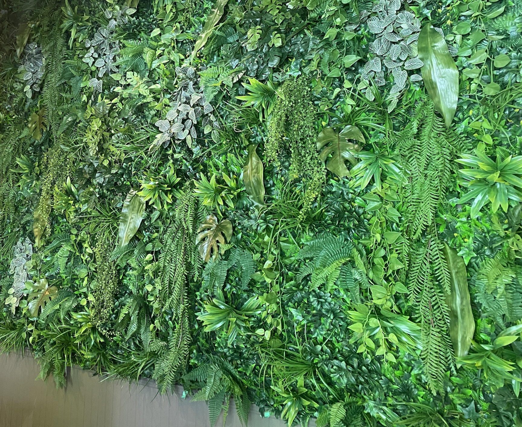 Artificial green wall featuring a vibrant mix of faux ferns, ivy, monstera leaves, and cascading greenery for a lush, natural look.