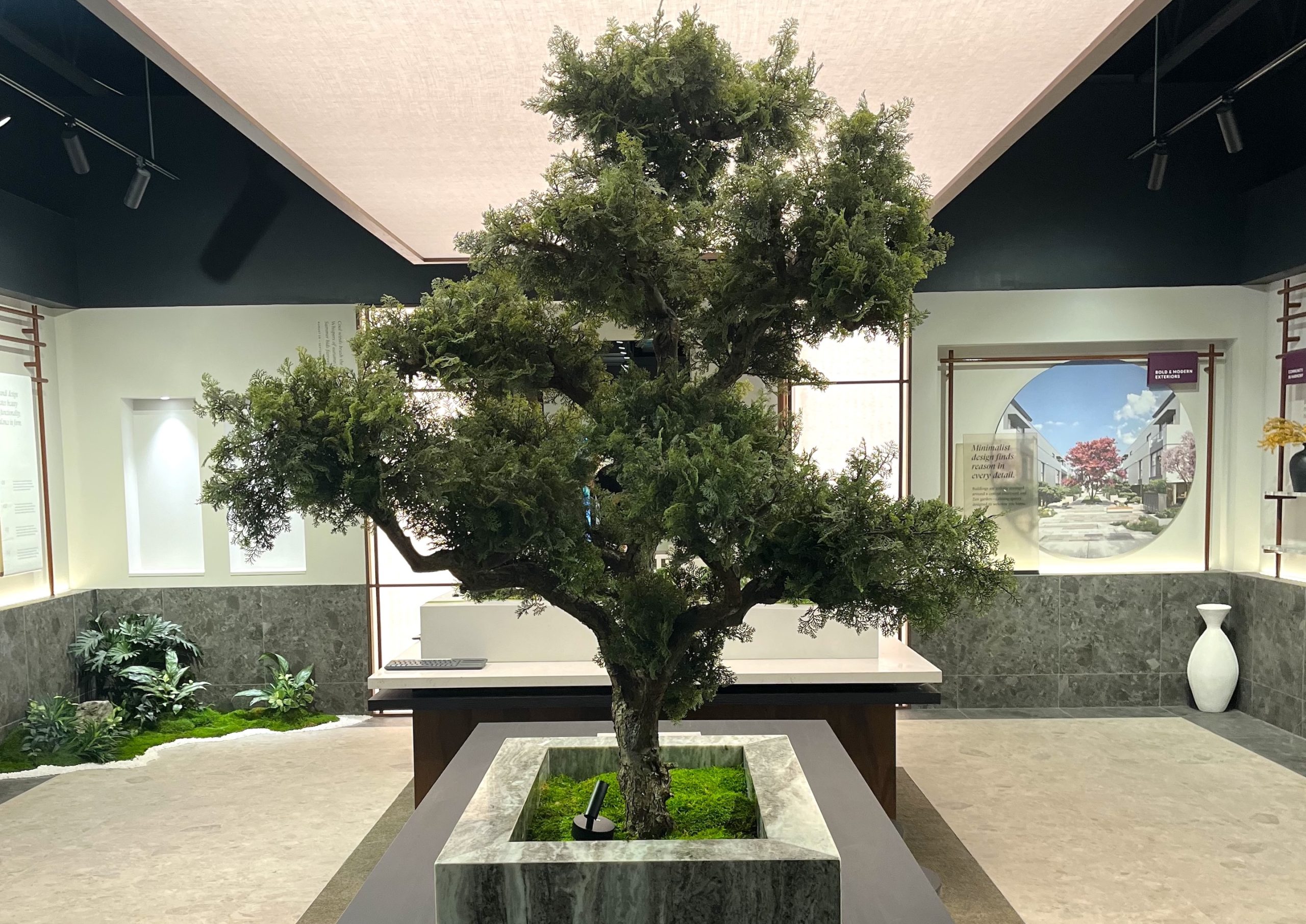 Faux bonsai tree in a sleek marble planter, creating a striking focal point in a modern showroom. Features lifelike foliage and detailed branching for a natural look.