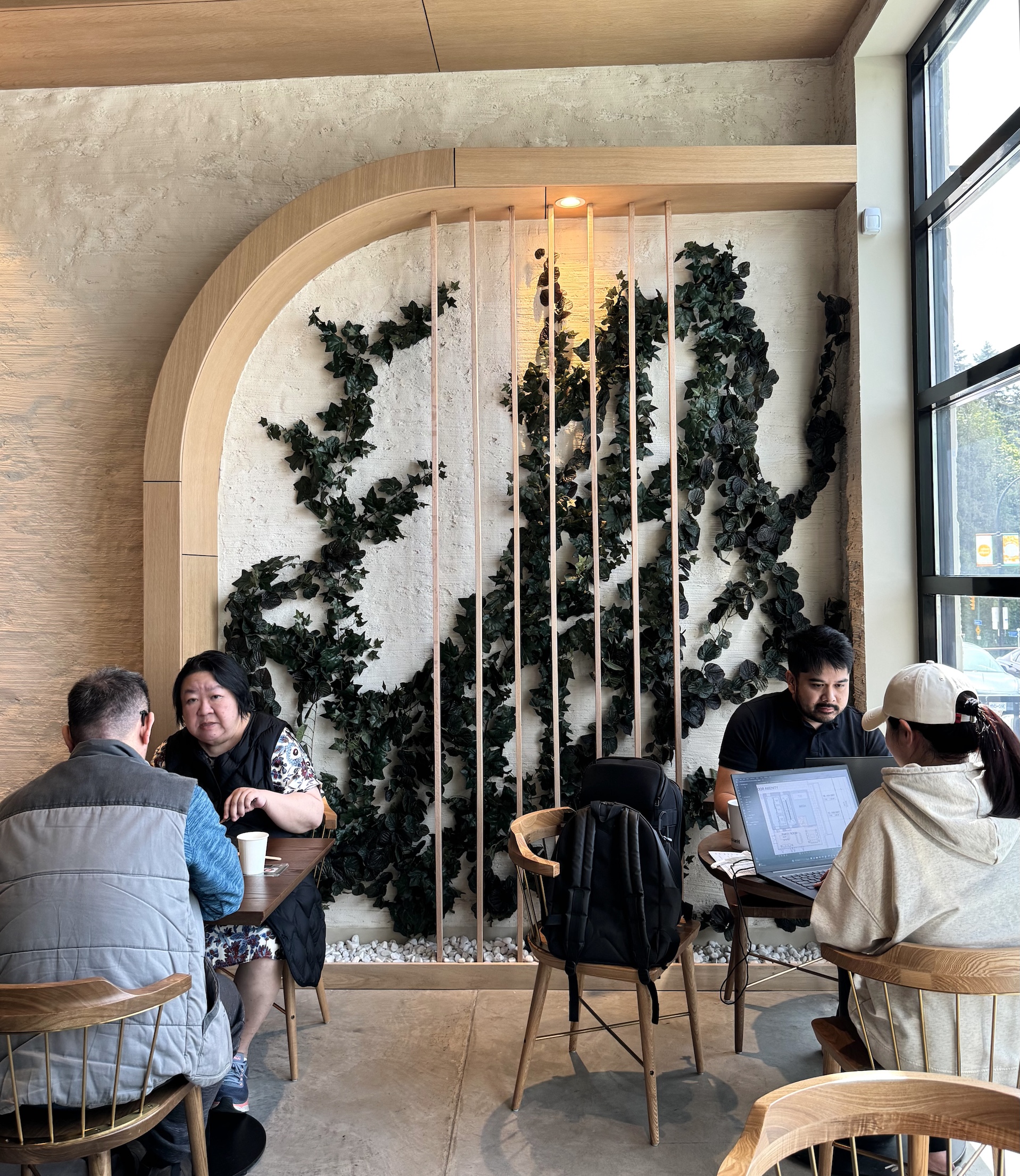 Faux ivy wall installation in a modern café with wood and stone accents. Features an organic greenery design framed by curved wooden slats for a natural aesthetic.