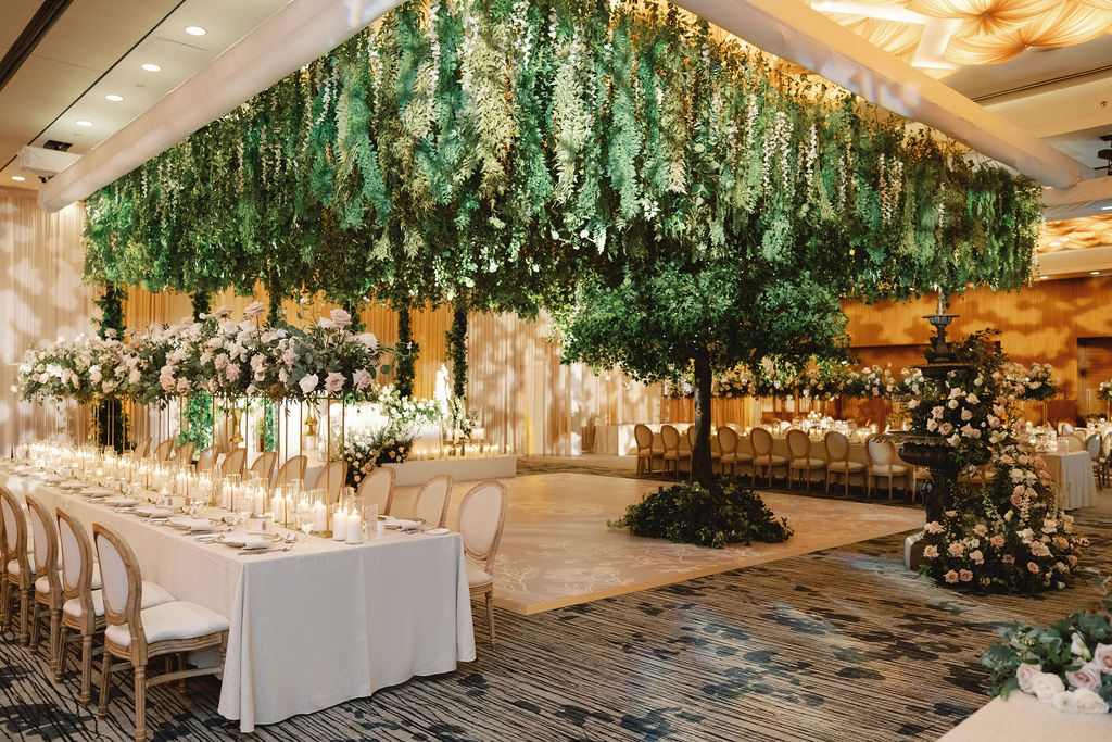 A luxurious wedding reception with a canopy of faux greenery, artificial trees, and elegant floral arrangements.