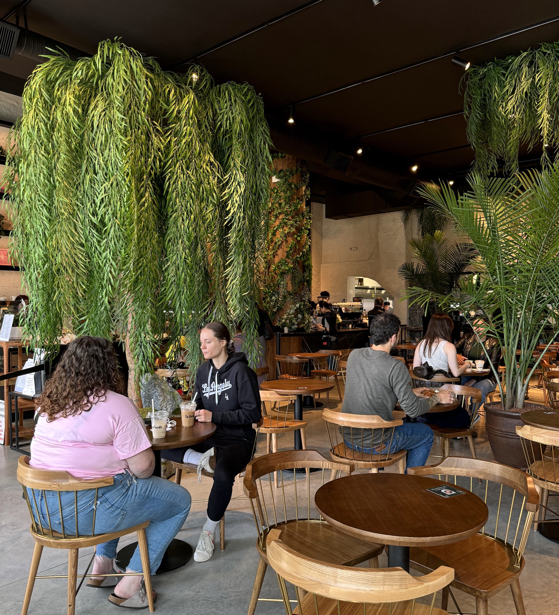 Faux willow tree with cascading greenery creates a lush focal point in a modern restaurant. Enhances the space with a biophilic design and natural ambiance.