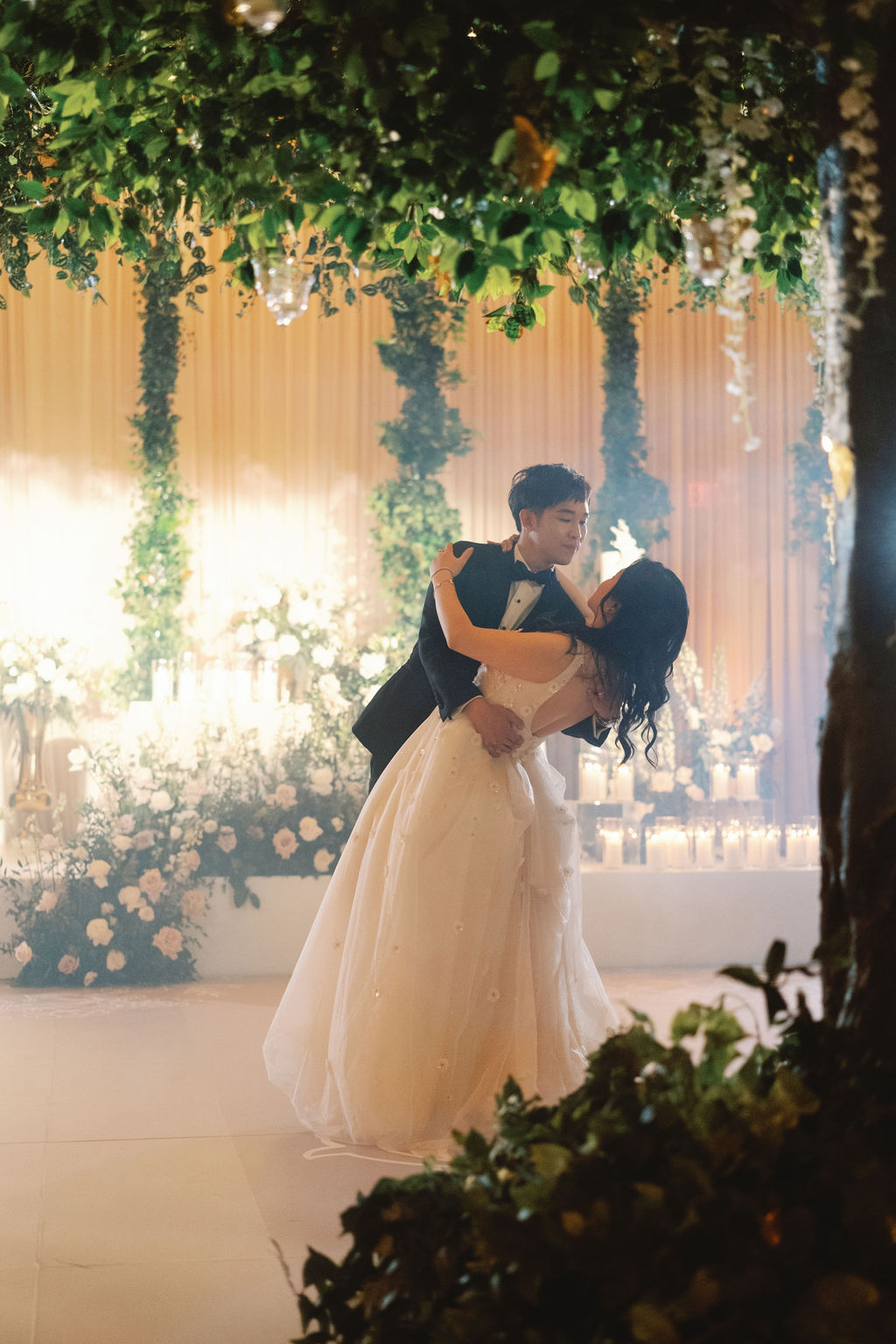 A bride and groom share a romantic dance under lush greenery and soft candlelight at a hotel wedding.