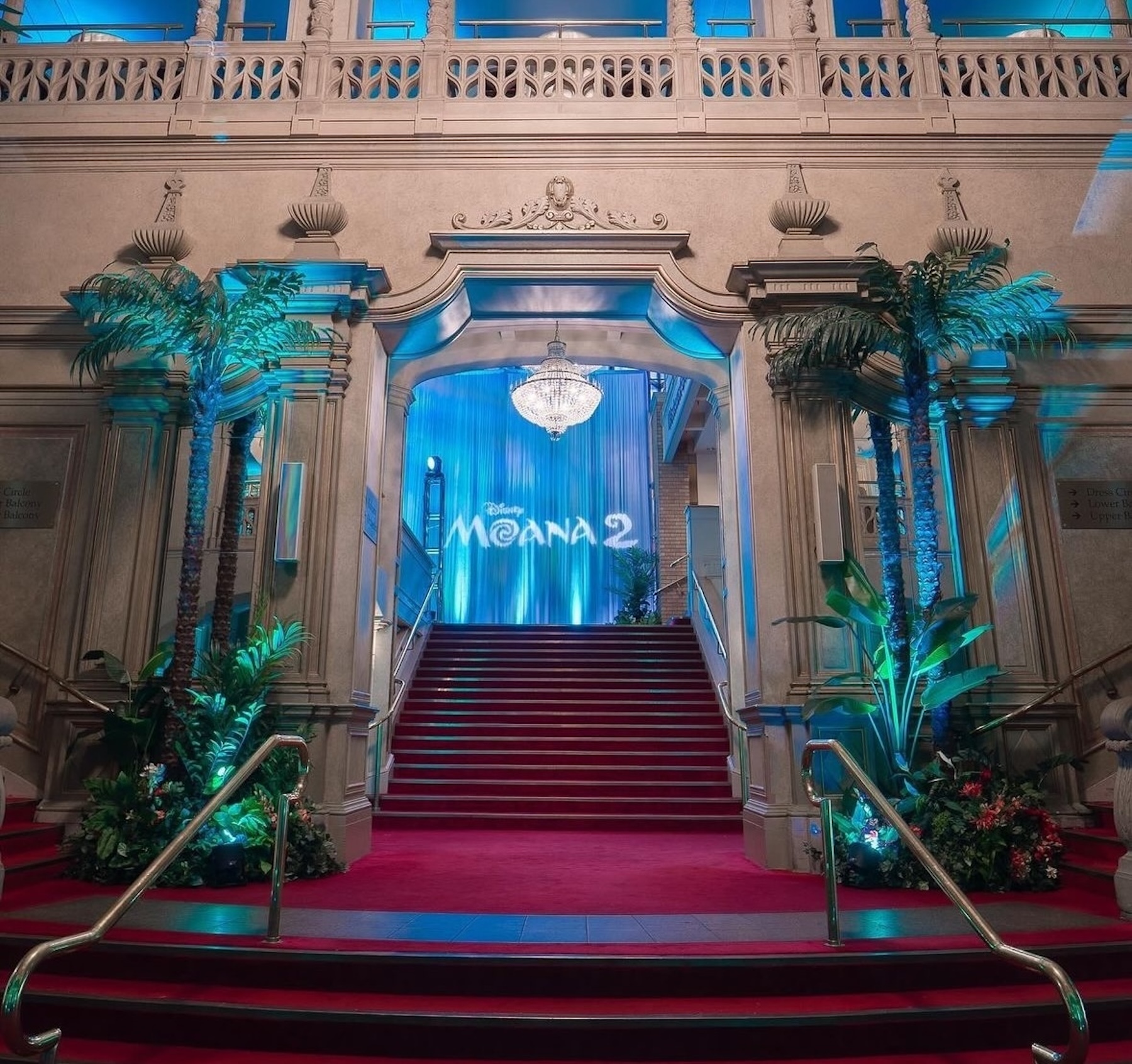 A grand event entrance featuring tropical palm trees, lush greenery, and blue lighting for a Moana-themed celebration.