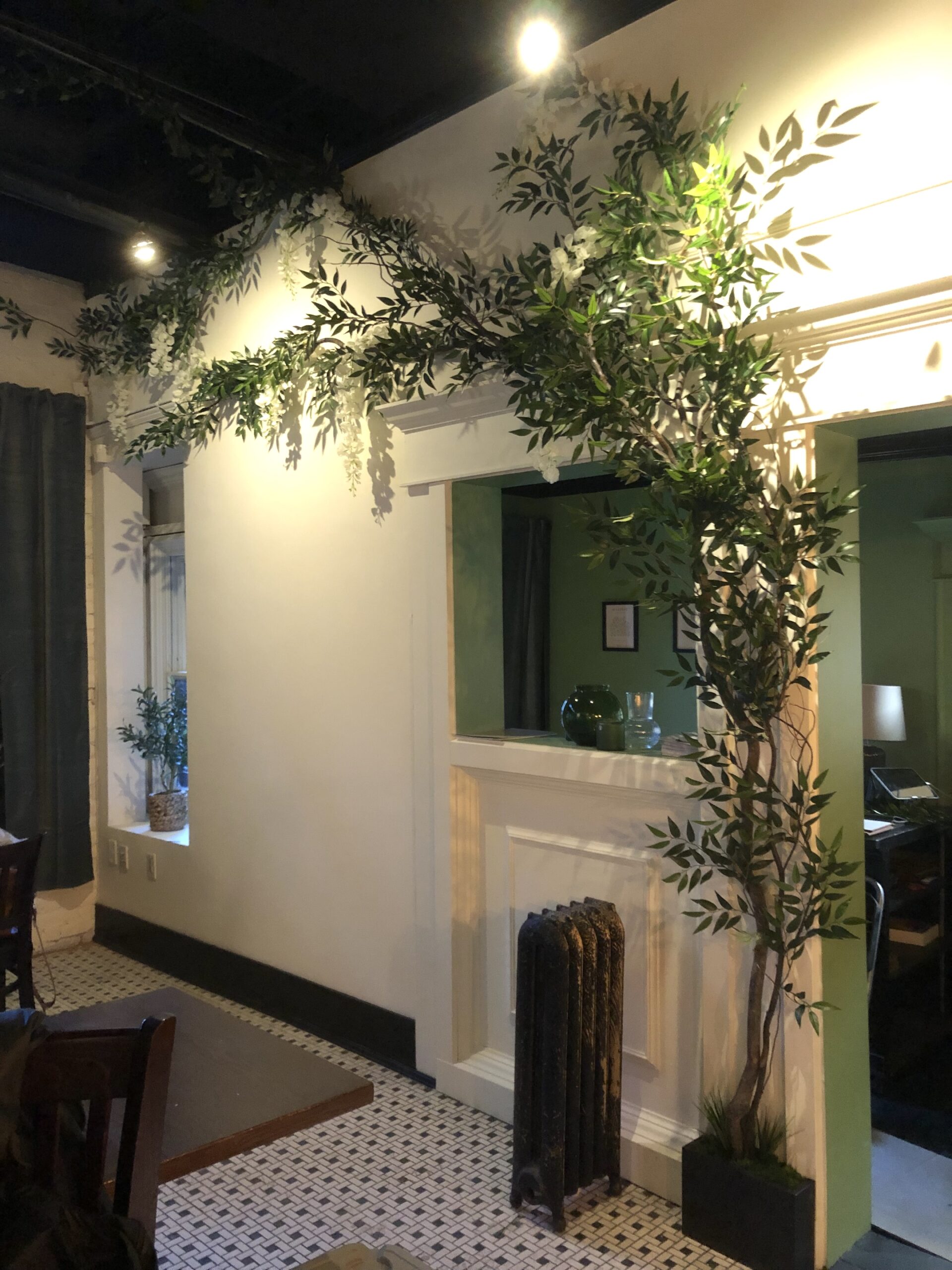 Artificial greenery installation at Petrichor Restaurant in Vancouver, featuring lush vines and foliage decorating a white wall and archway.