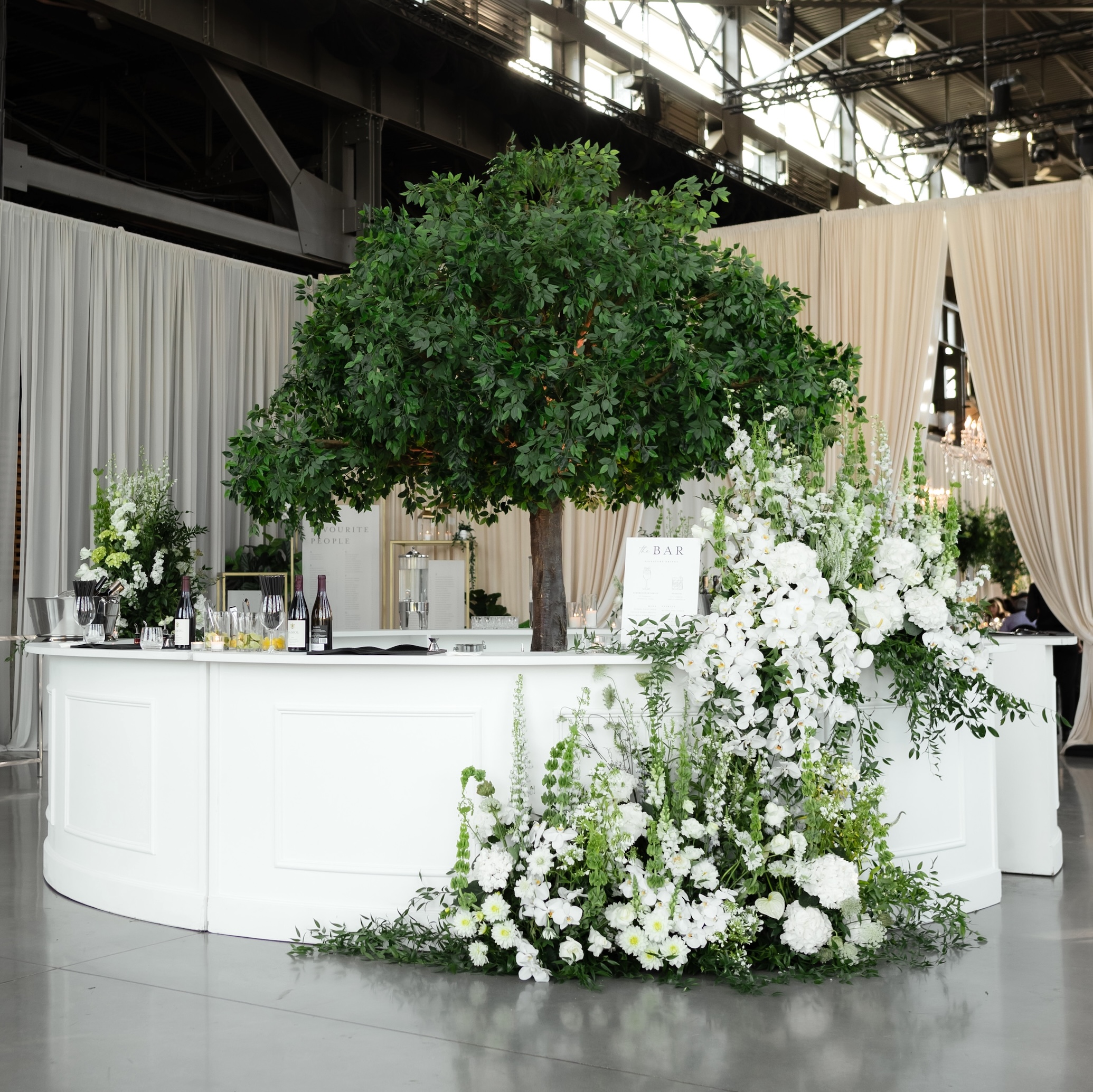 A white wedding bar with lush floral arrangements and an artificial tree centerpiece at Rocky Mountaineer Vancouver.