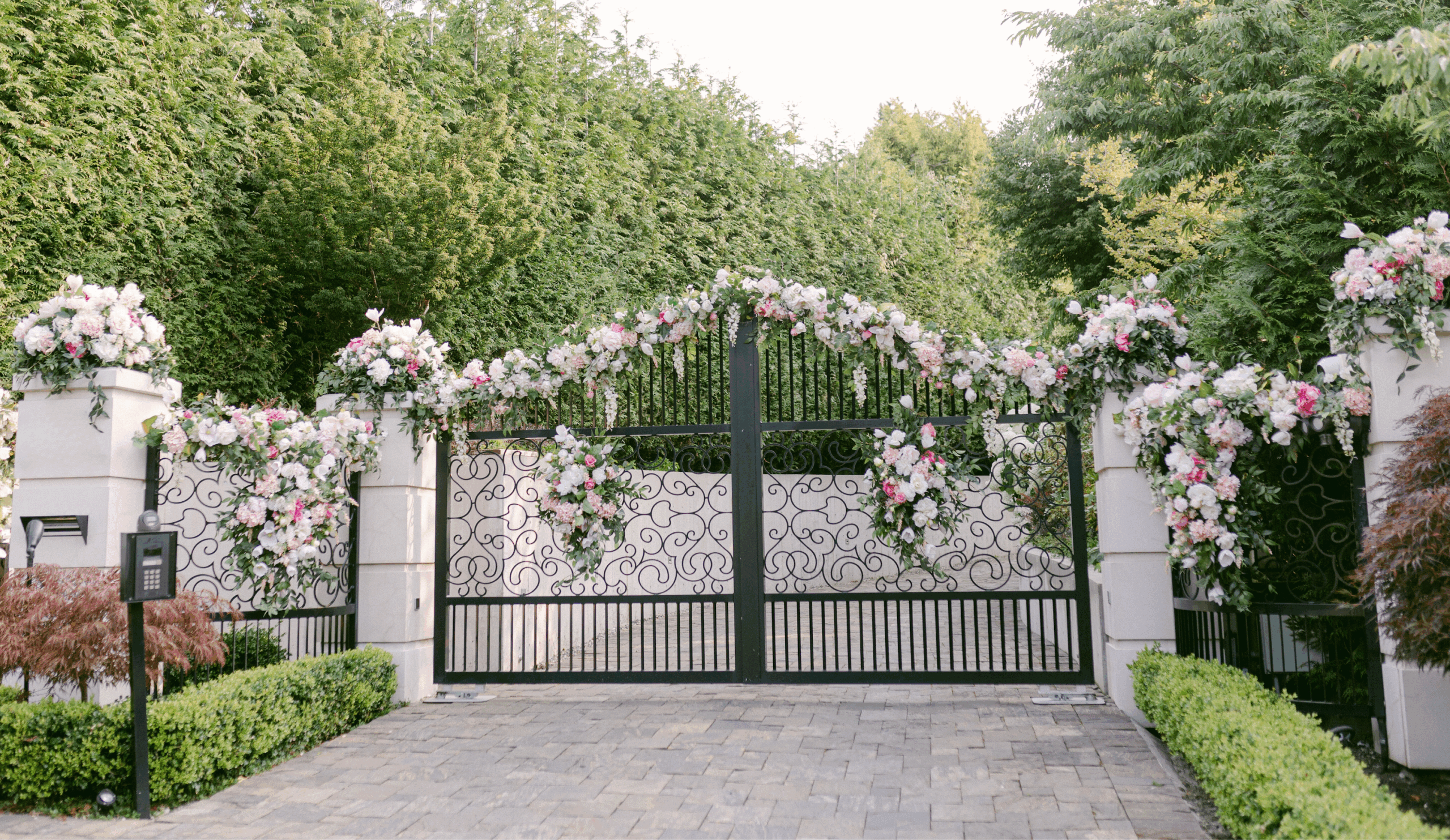 A grand wrought iron gate adorned with lush pink and white floral arrangements, creating a romantic entrance for a luxury wedding.