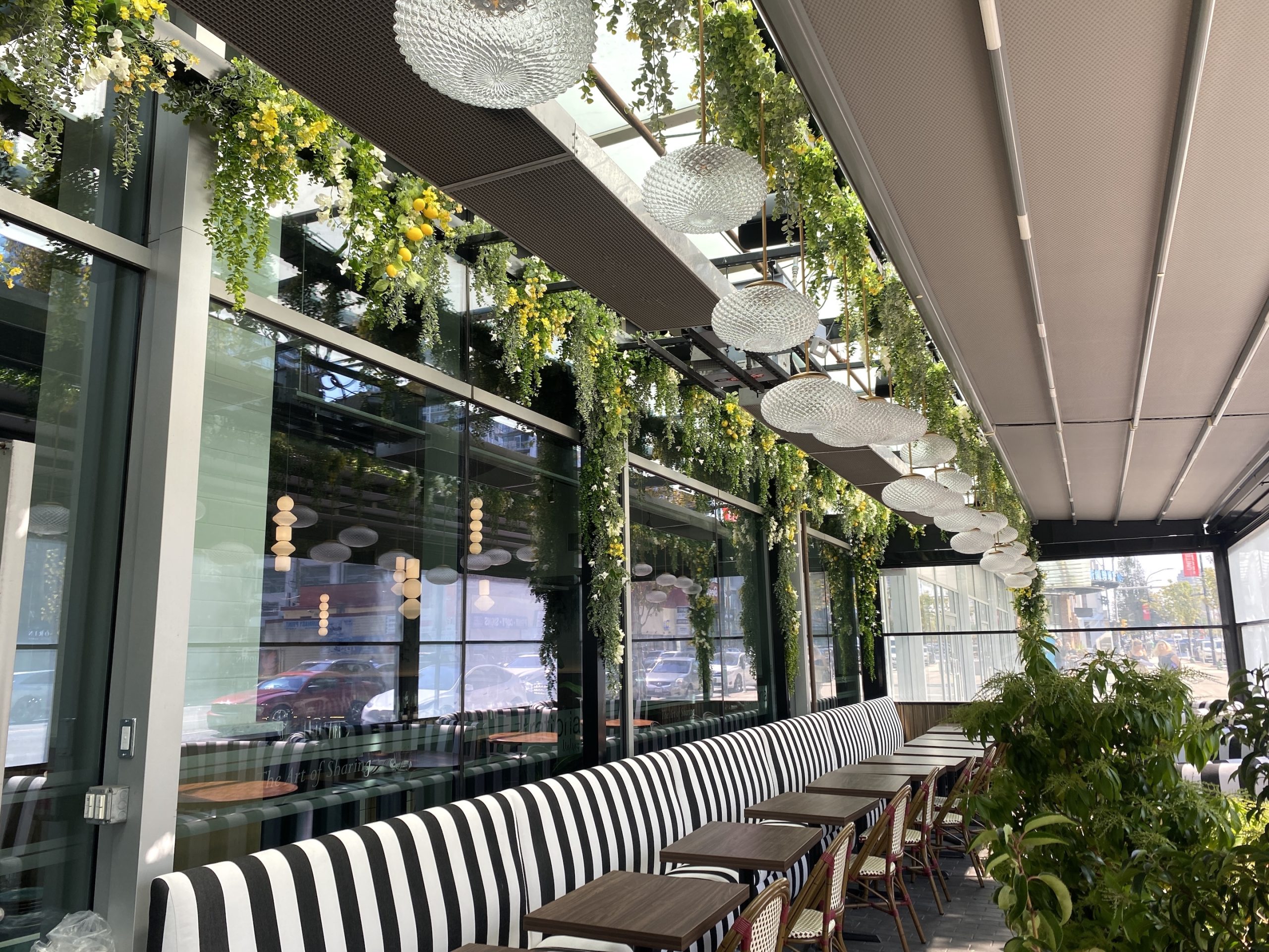 Artificial greenery cascades from the ceiling of a stylish patio, featuring lush vines, yellow blooms, and faux lemons. Crystal pendant lights add a touch of elegance to the dining space.